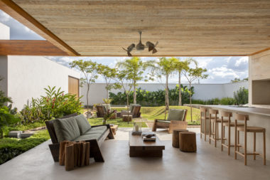 área externa da casa com sofá, mesa de centro, banca e vista para o jardim