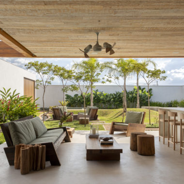 área externa da casa com sofá, mesa de centro, banca e vista para o jardim