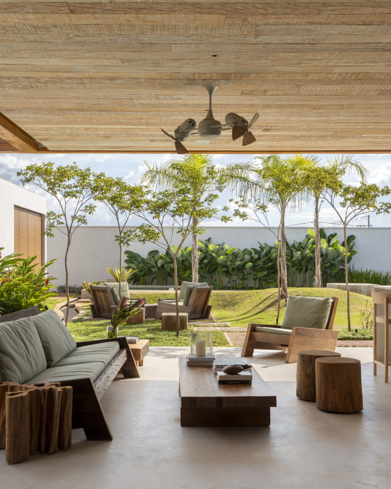 área externa da casa com sofá, mesa de centro, banca e vista para o jardim