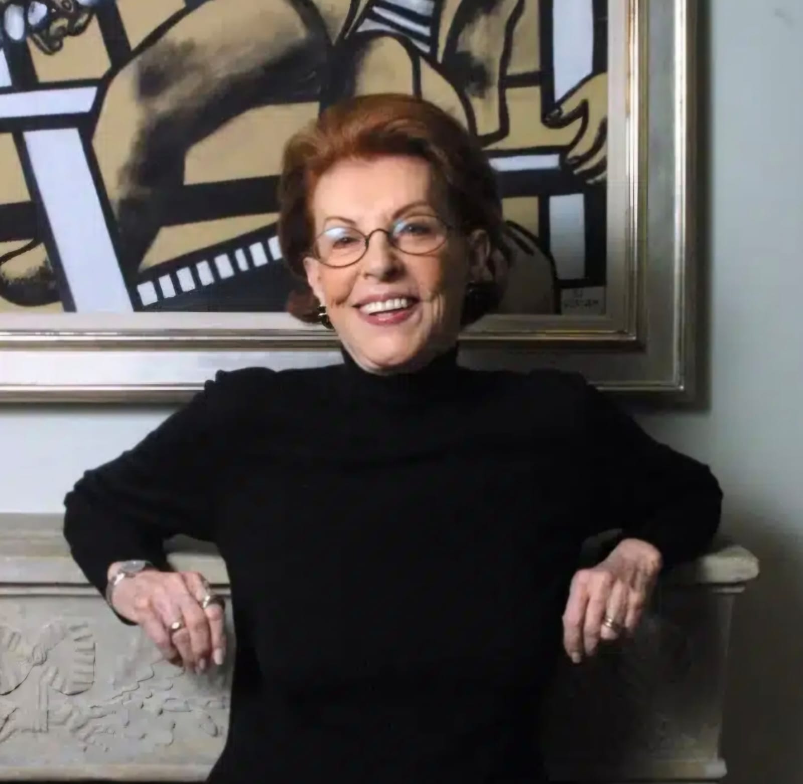 foto colorida de uma mulher branca com roupa preta sentada e sorrindo