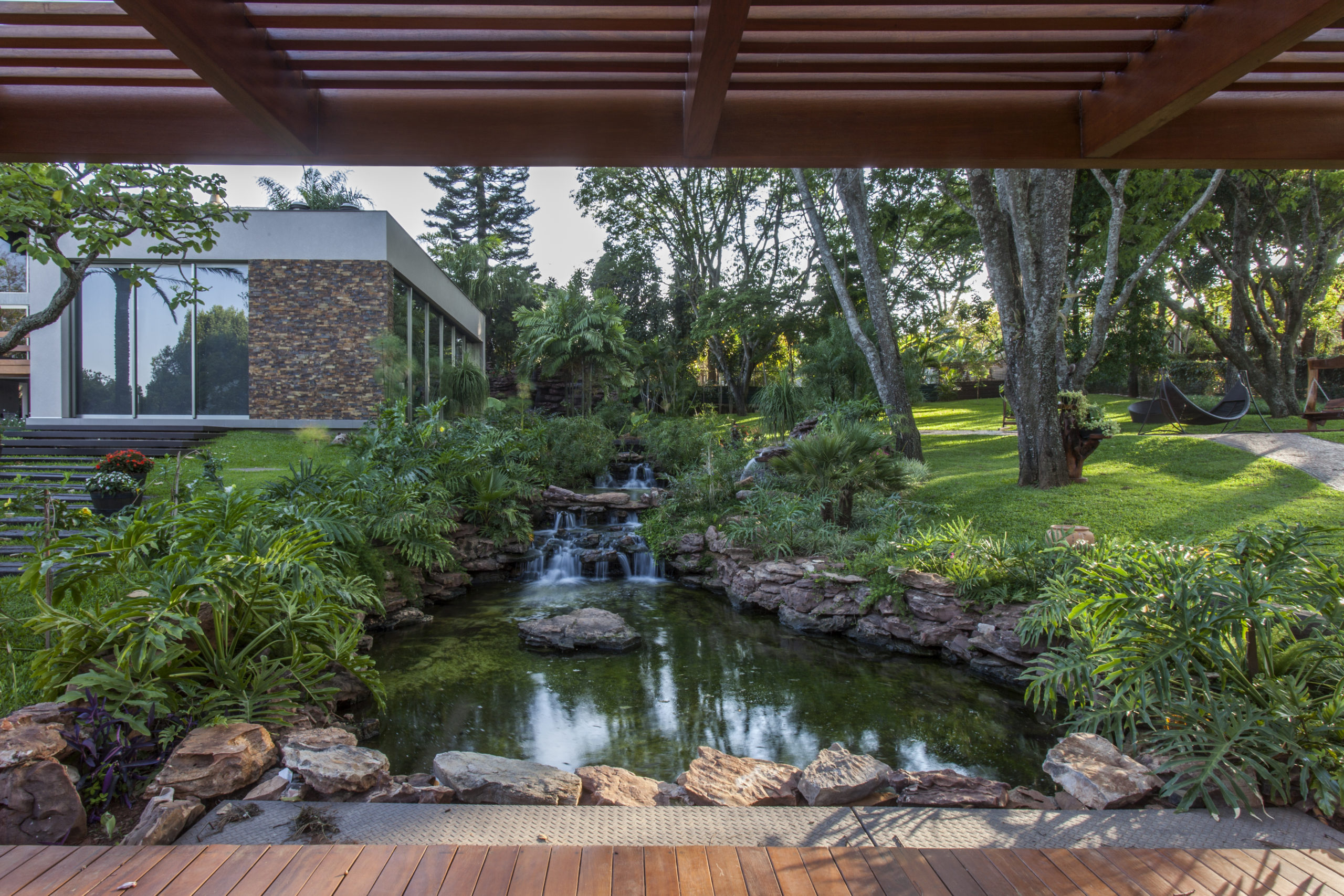 na foto uma casa com lago, pedras e árvores