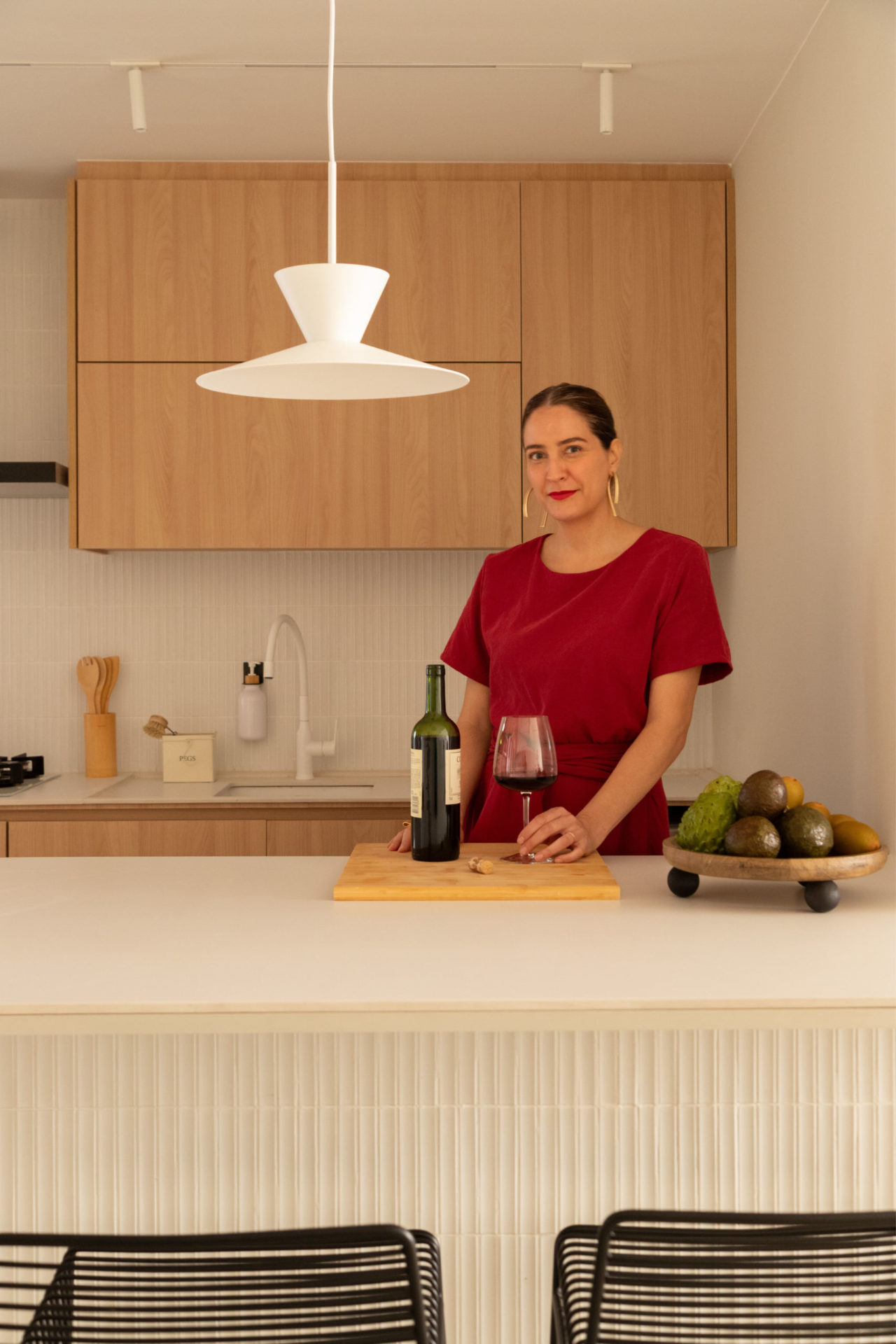 na foto mulher branca, alta, de cabelo castanho e preso na cozinha com uma garrafa de vinho