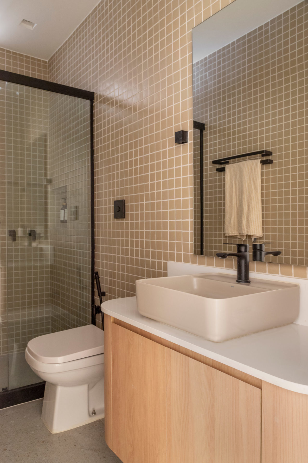 na foto banheiro com bancada branca, vaso branco, armário de madeira clara e box