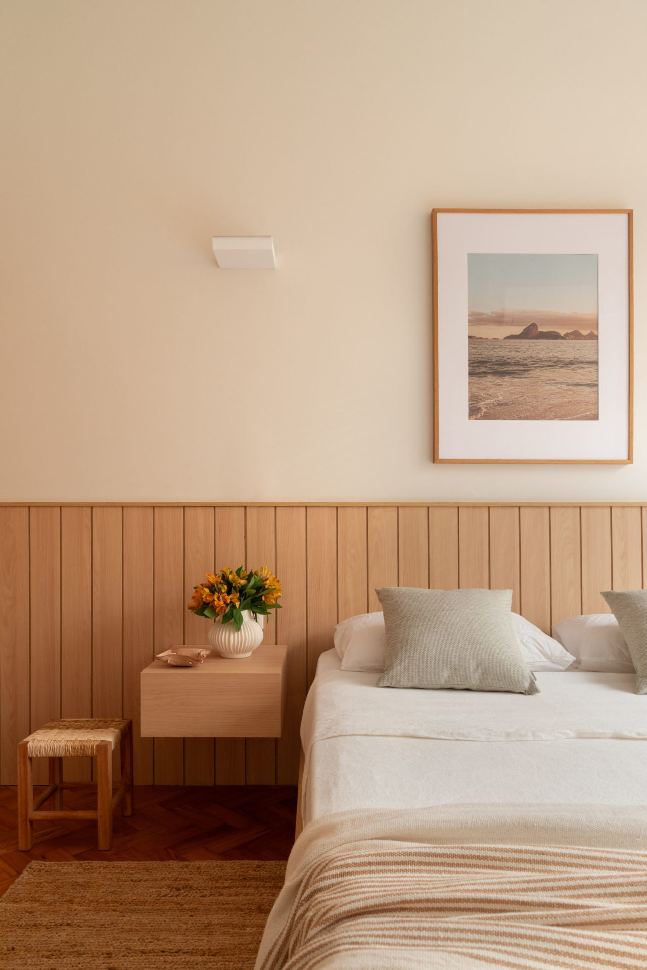 na foto cama com mesinha de cabeceira e vaso com flores. quarto em tons claros