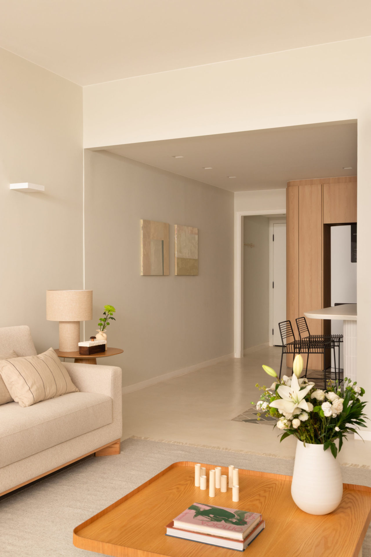 na foto uma parte da sala de estar com sofá off-white, vaso com flores e a bancada da cozinha