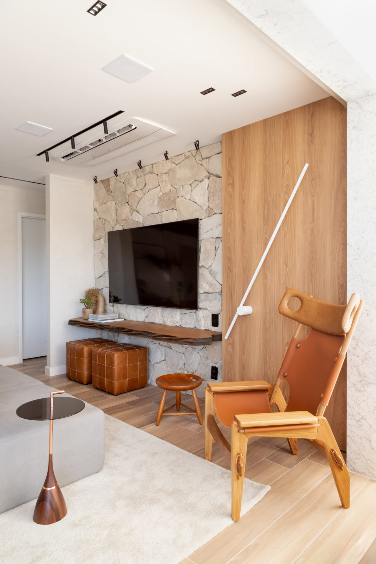 na foto sala com TV na parede, cadeira e puffs