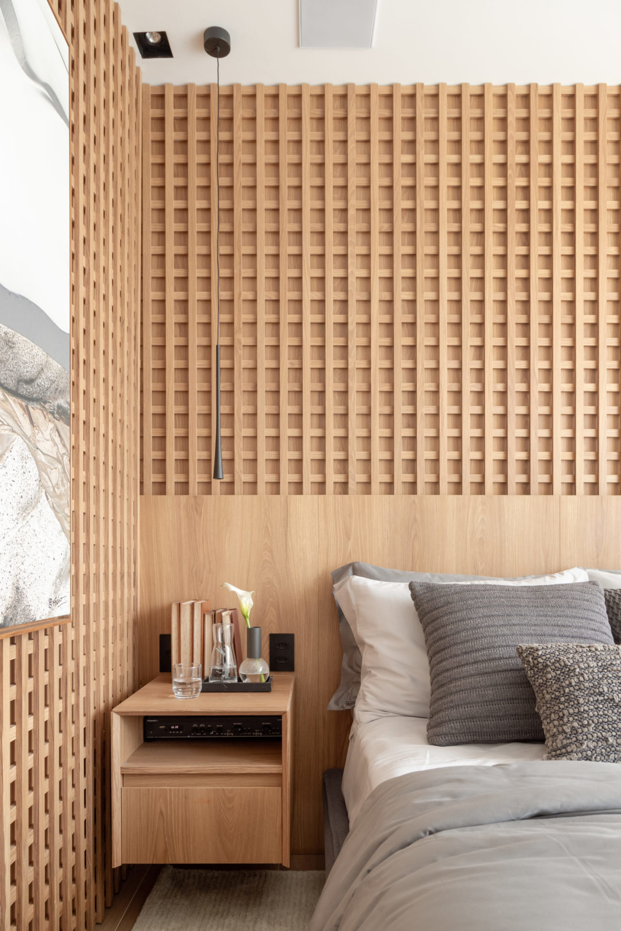 na foto um quarto com cama, mesinha de cabeceira e muxarabi em duas paredes