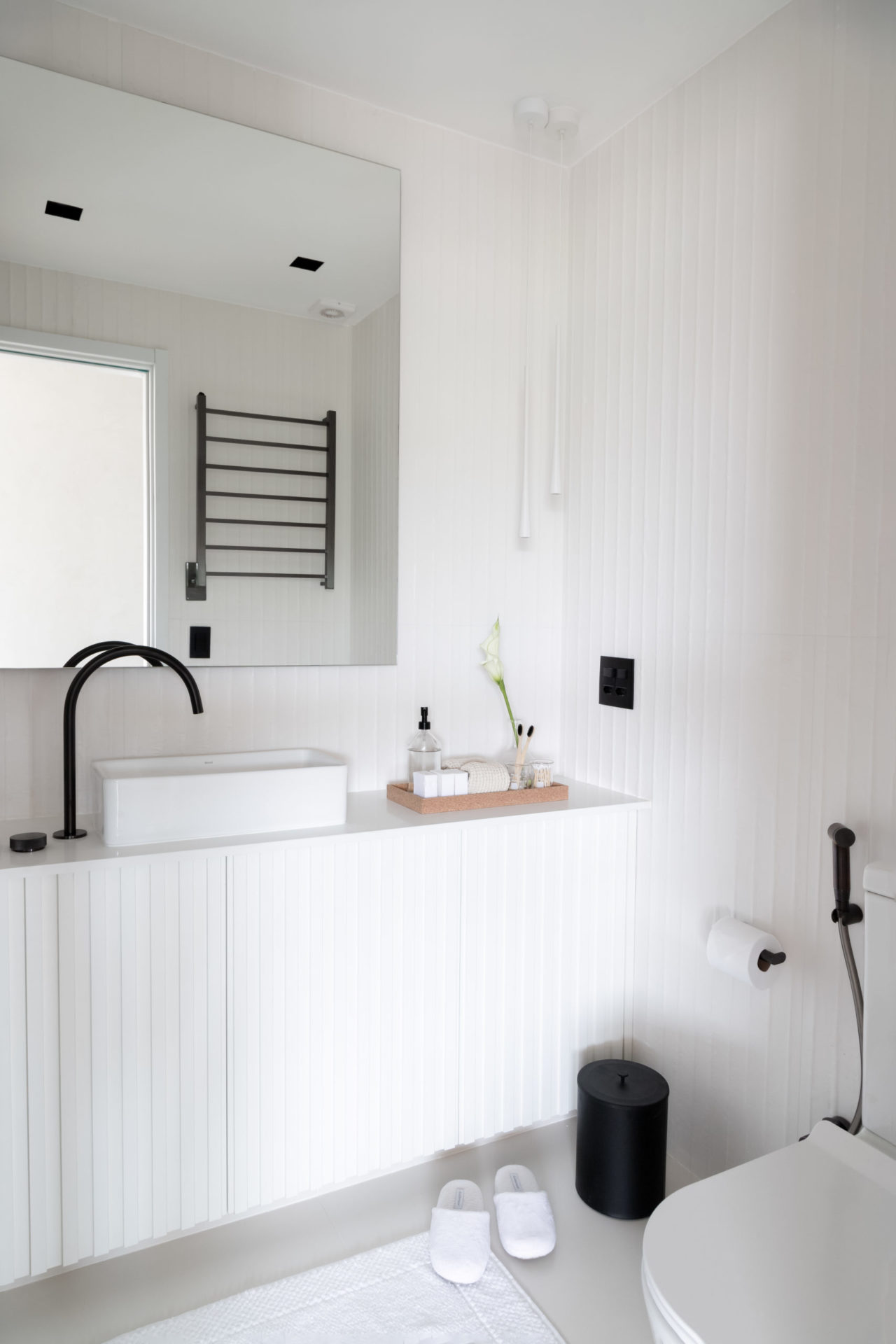 na foto um banheiro todo branco com bancada e chuveirinho 