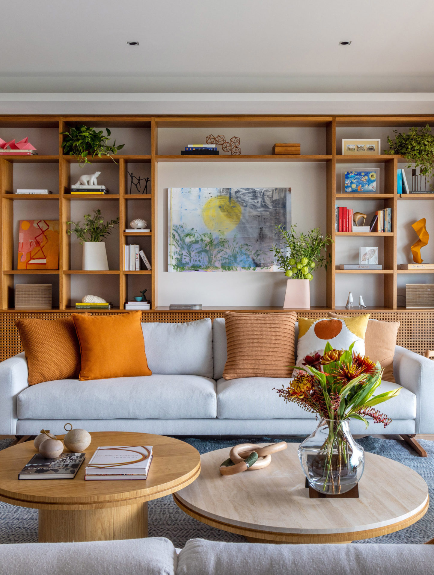 na foto sala de estar com sofá branco, almofadas, mesa de centro e estante na parede