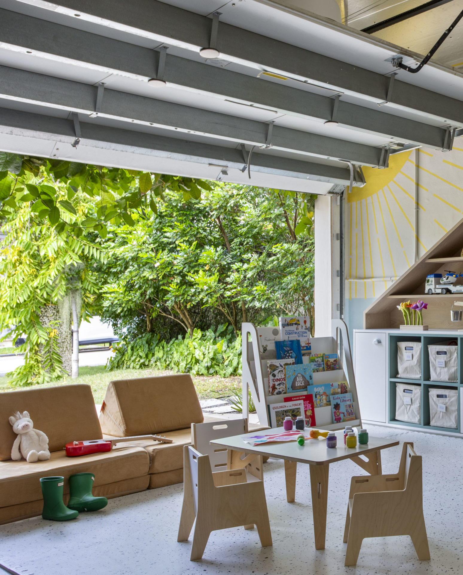 na foto uma brinquedoteca com sofá, casinhas de madeira, mesinha de madeira