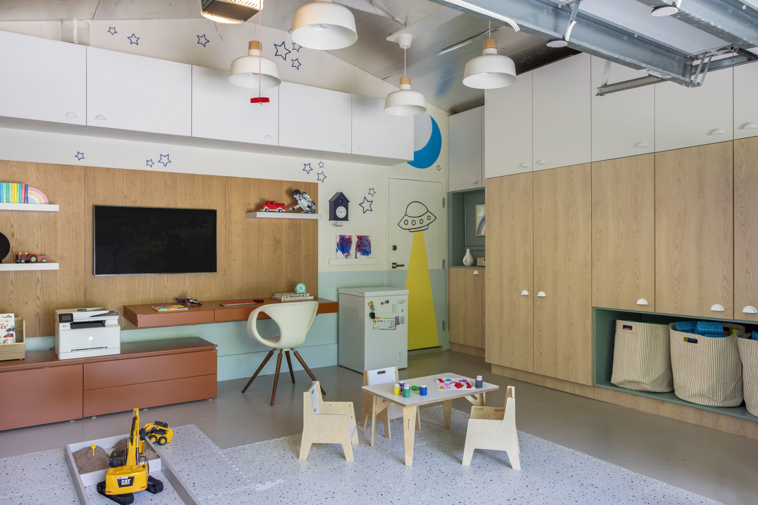 na foto uma brinquedoteca com espaço para uma mesa de trabalho e televisão presa na parede e armários