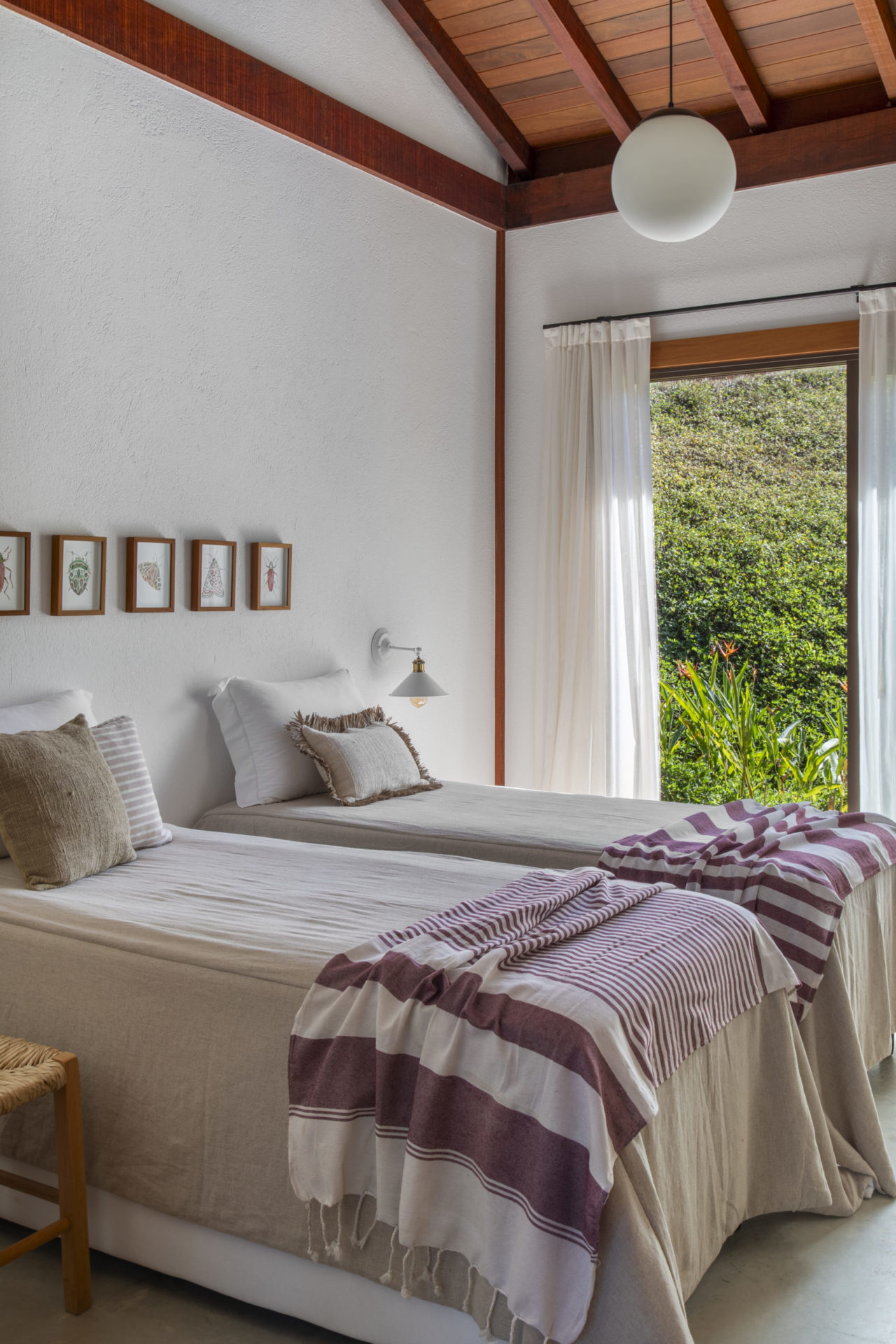 na foto duas camas de solteiro, quadros pequenos na parede e janela para o verde