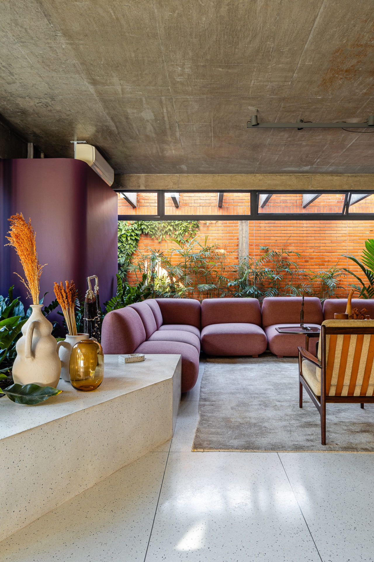 na foto uma sala de estar com sofá ilha, poltrona e varanda com plantas