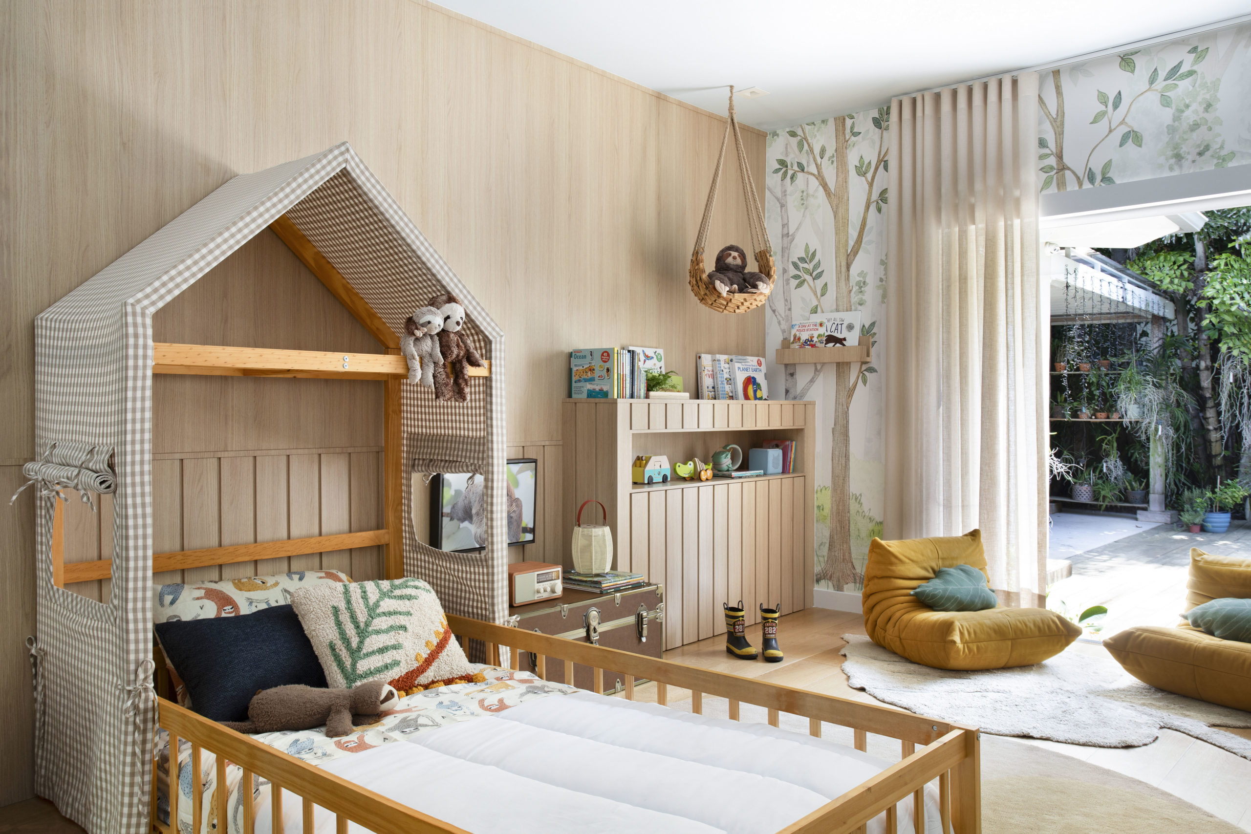 na foto quarto de criança com cama com cabeceira em formato de casa, uma preguiça de pelúcia pendurada e cortina