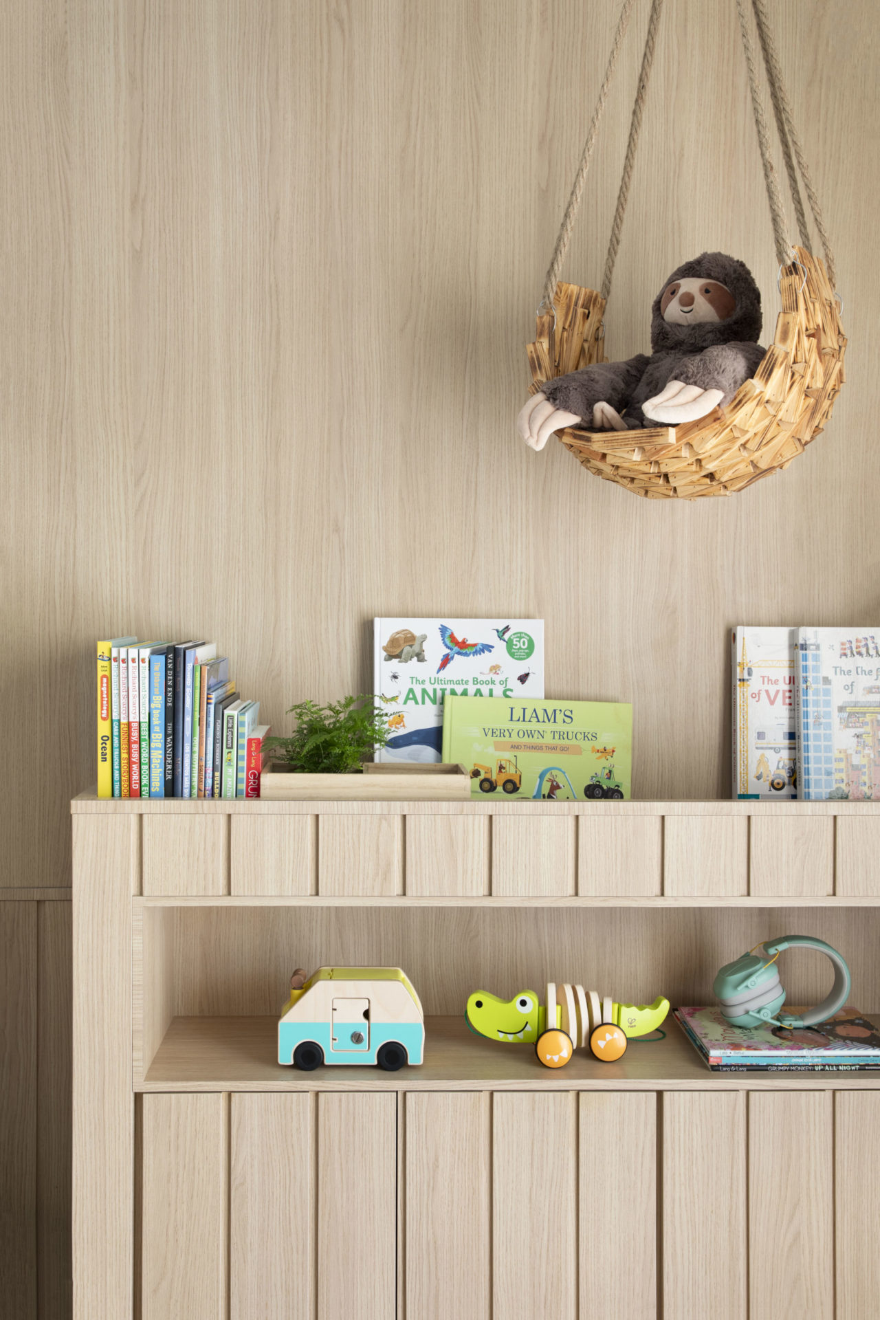 na foto quarto infantil com estante com brinquedos e livros e uma preguiça de pelúcia pendurada