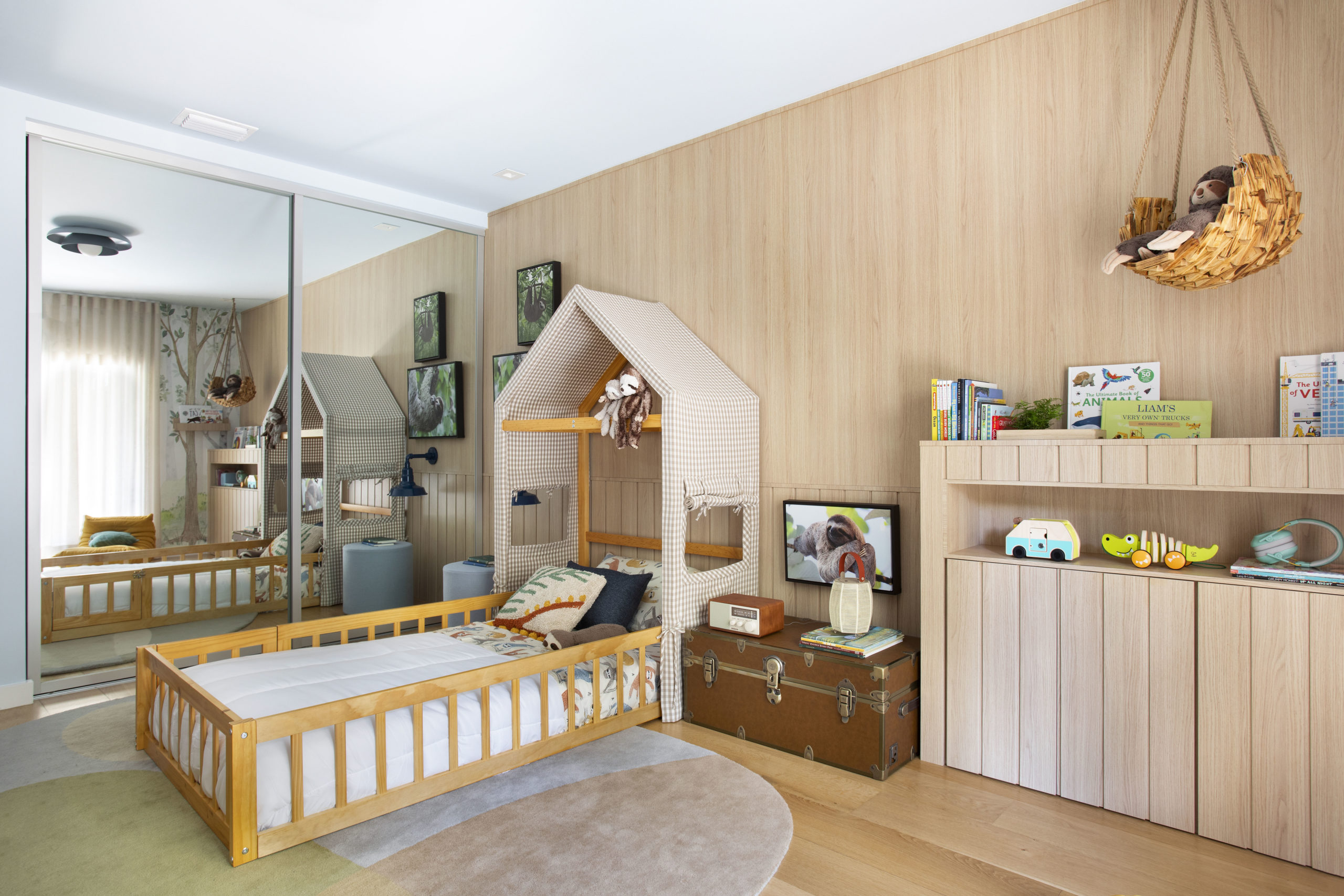 na foto quarto infantil com cama com cabeceira em formato de casa, cômoda, armário espelhado e baú