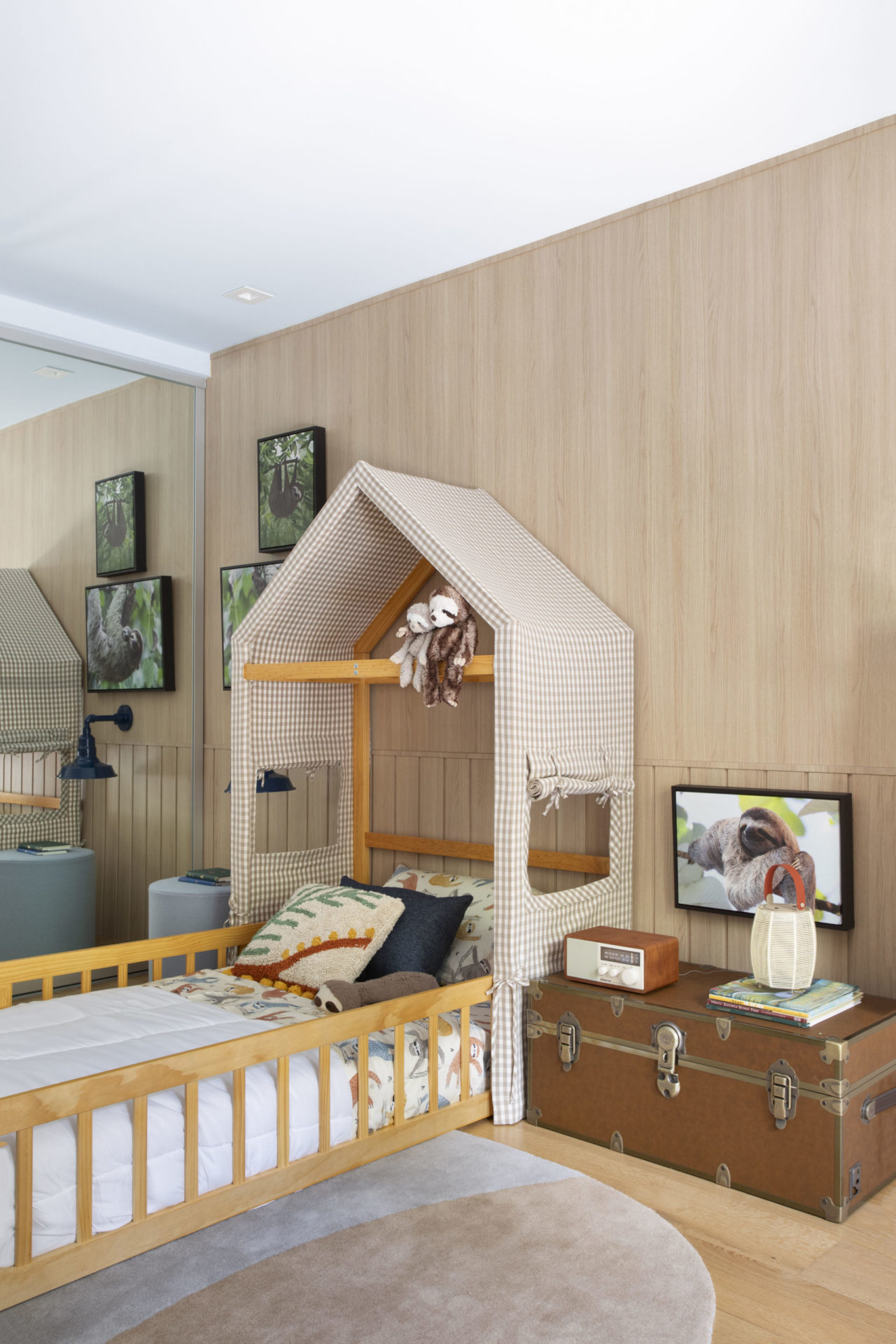 na foto quarto infantil com baú de madeira, cama com cabeceira em formato de casa e armário espelhado