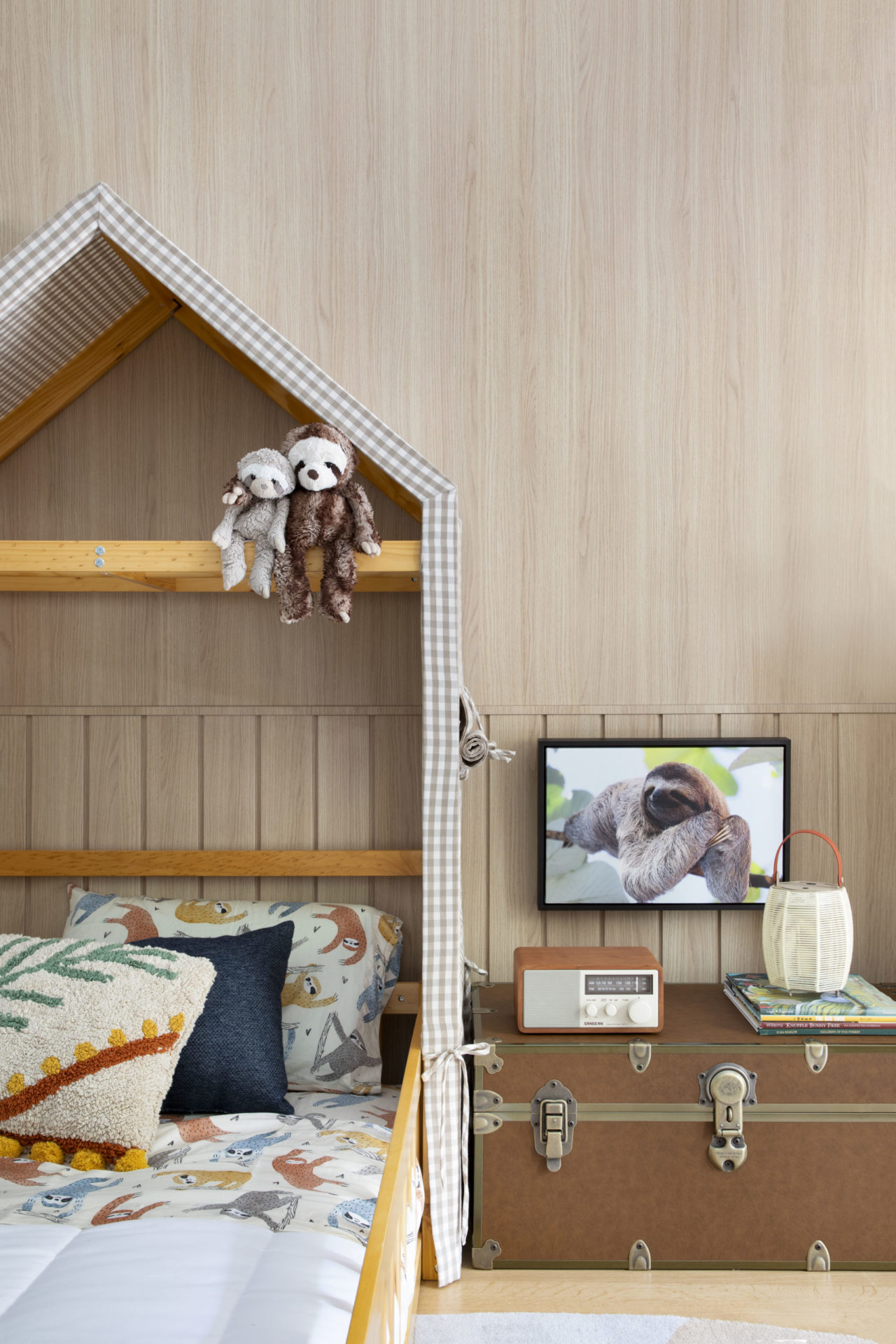 na foto quarto infantil com cama com cabeceira em formato de casa, quadro de preguiça e baú de madeira