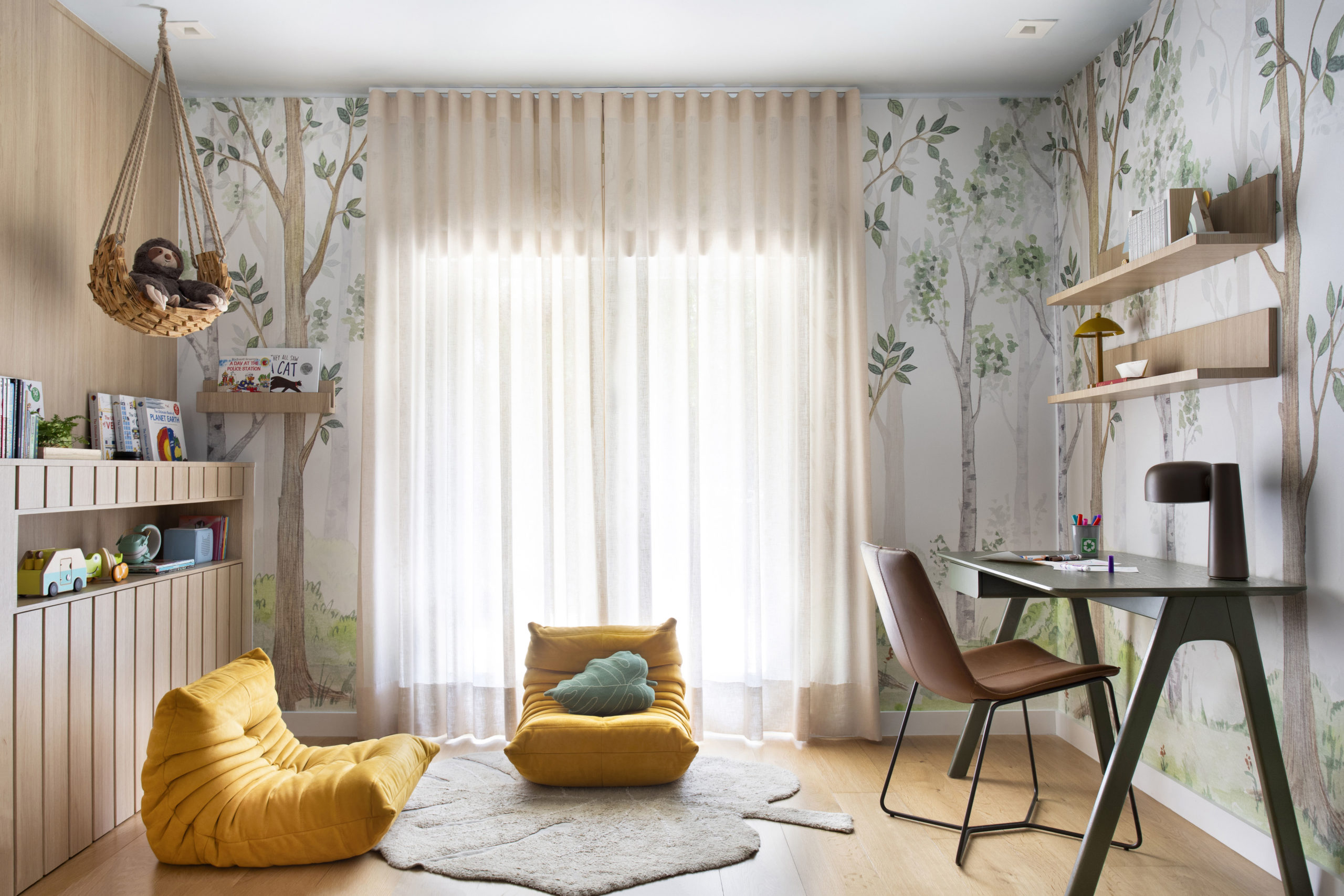 na foto quarto infantil com puffs, bicho preguiça de pelúcia, mesa de estudo e cortina