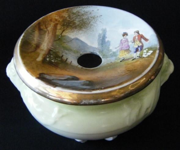 na foto objeto redondo na cor bege com furo no meio e com uma pintura de campo com duas pessoas