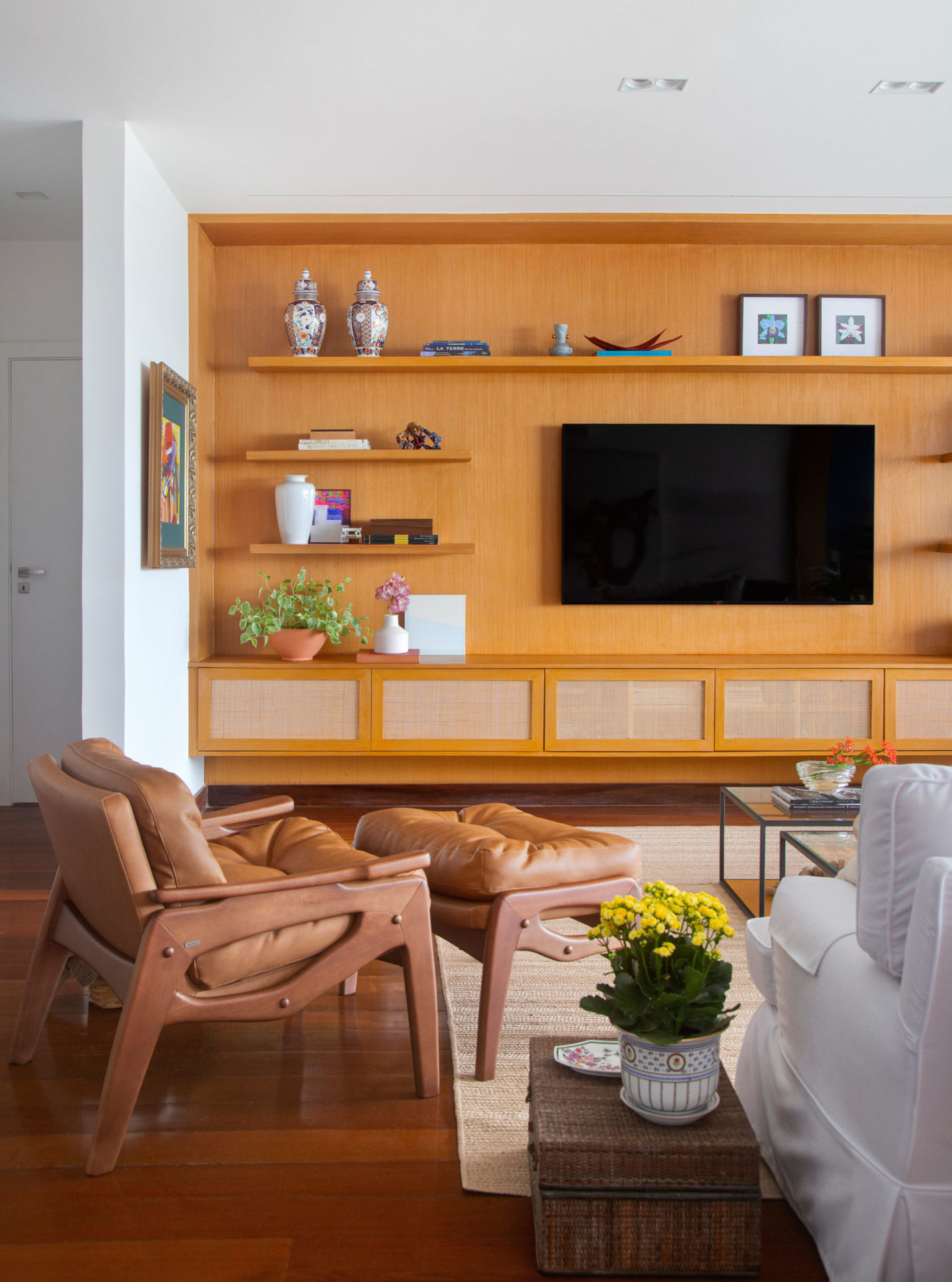na foto sala com poltrona de couro, sofá branco e painel de madeira com tv
