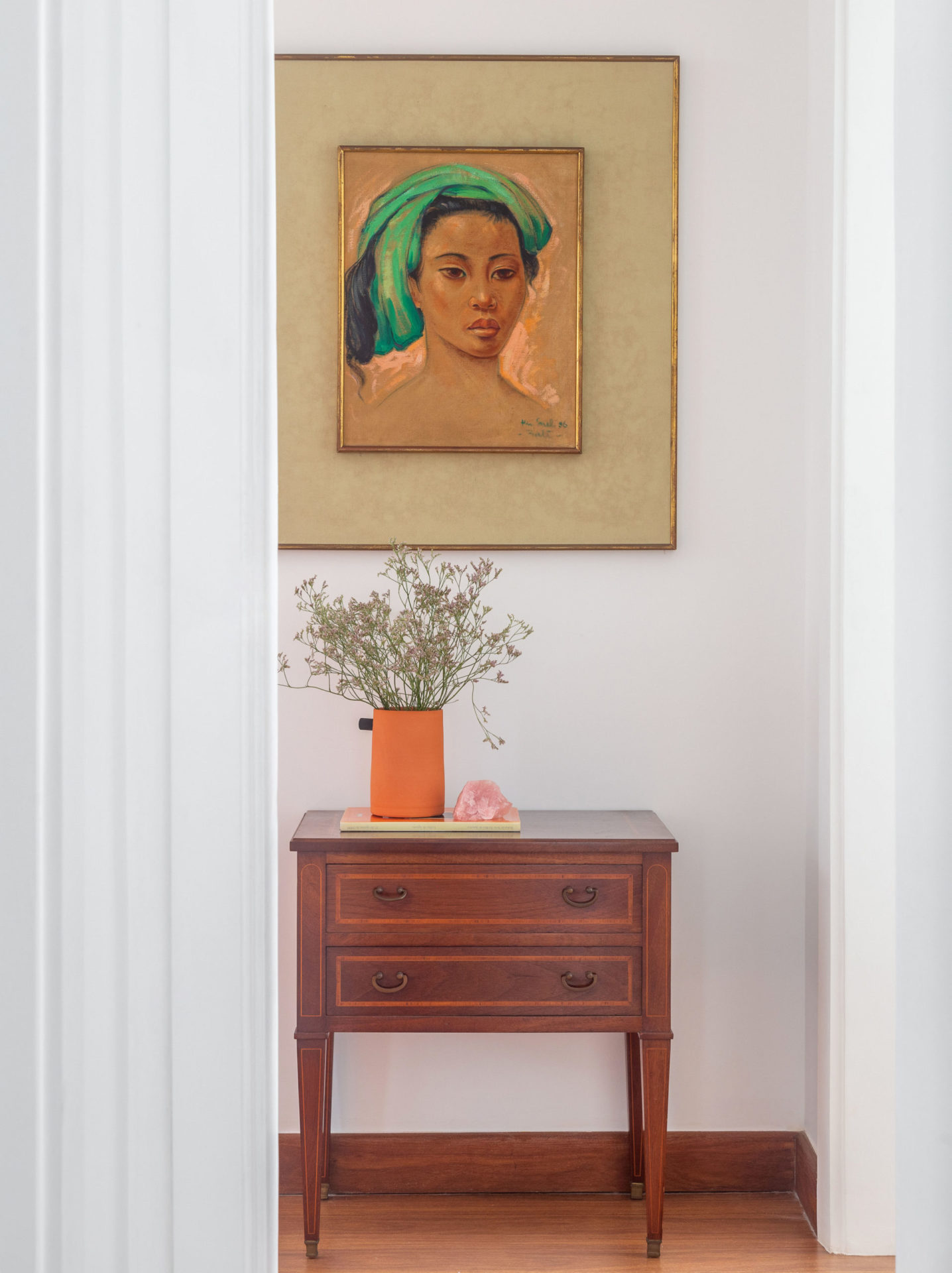 na foto mesinha de cabeceira com um vaso de flores e um quadro na parede