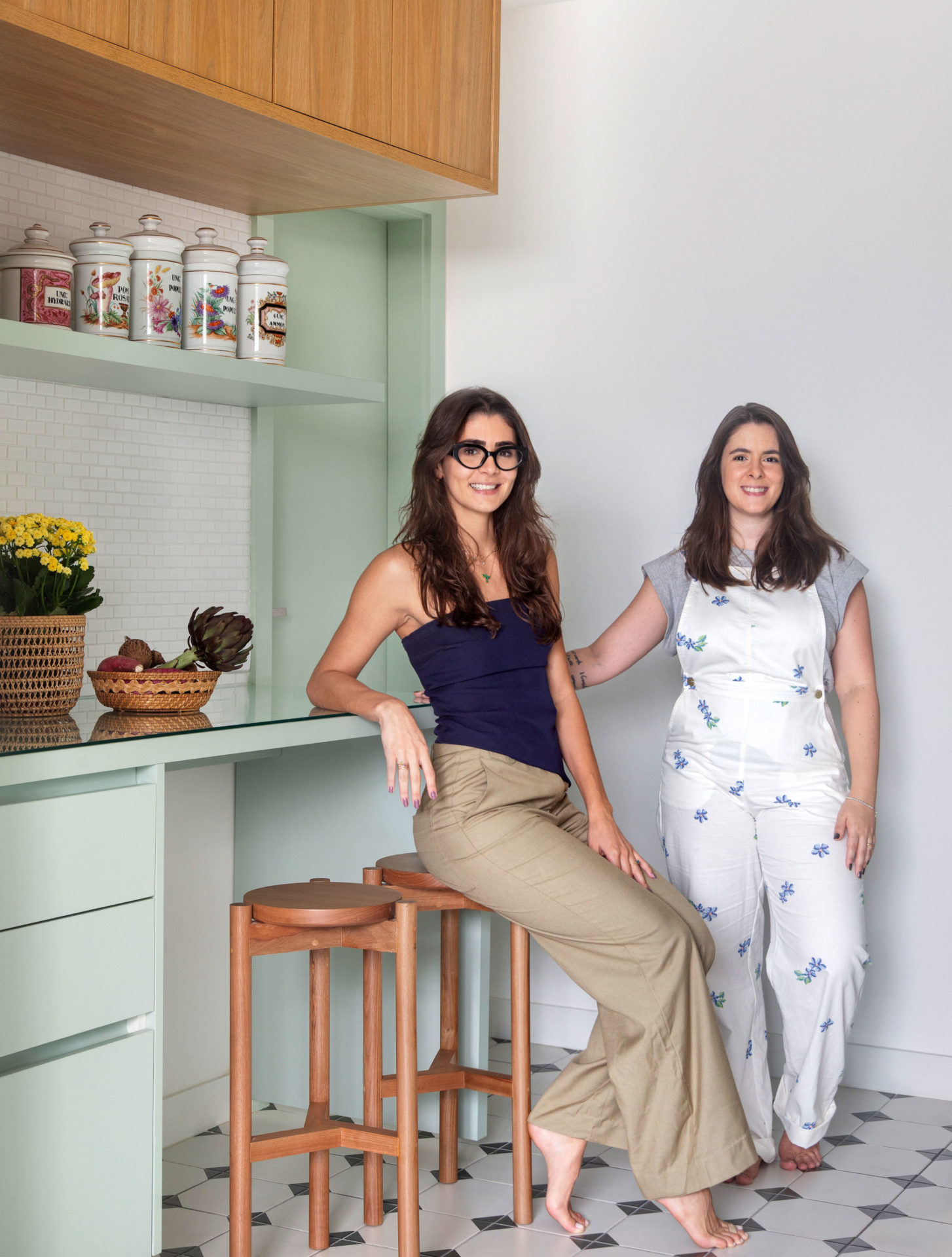 na foto duas mulheres brancas. uma sentada e a outra de pé