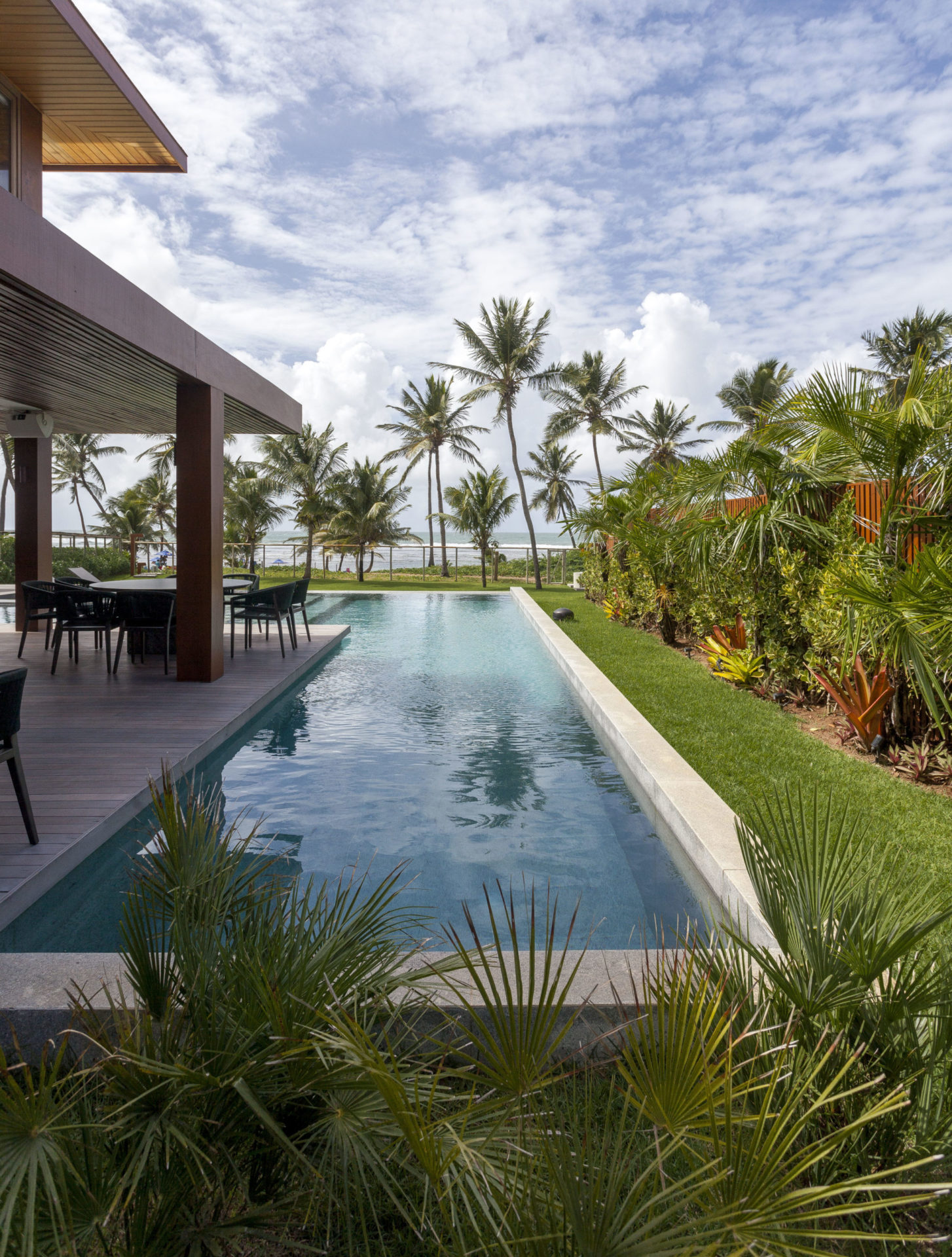 na foto casa de praia com piscina e muito verde como coqueiros