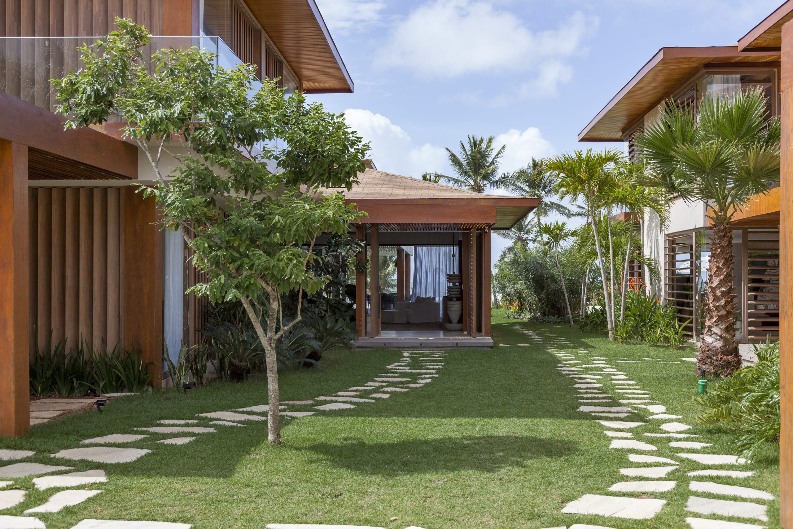 na foto casa de praia com muito verde e caminho de pedras