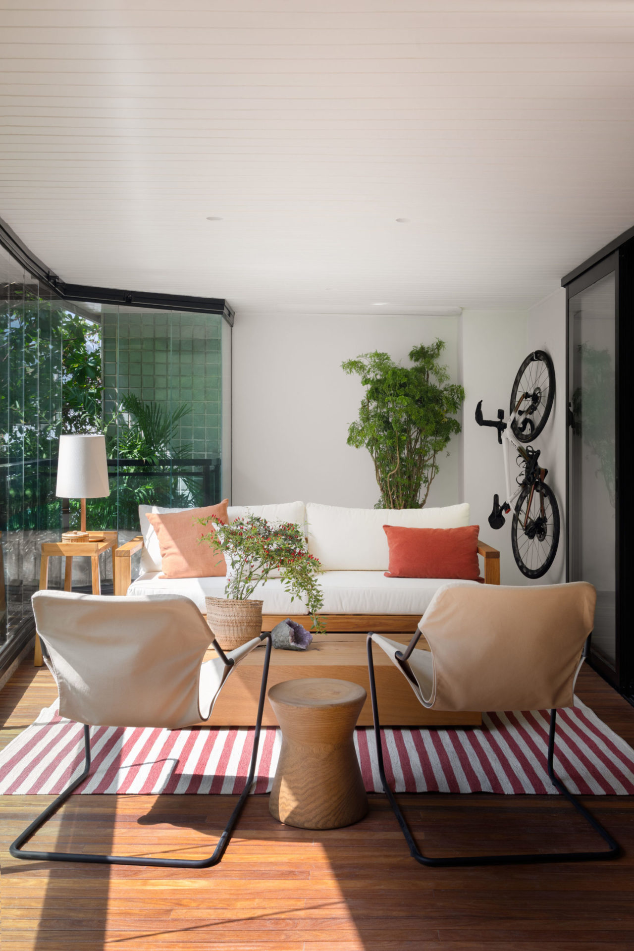 na foto espaço com duas poltronas brancas, um sofá branco, uma bicicleta presa na parede e plantas