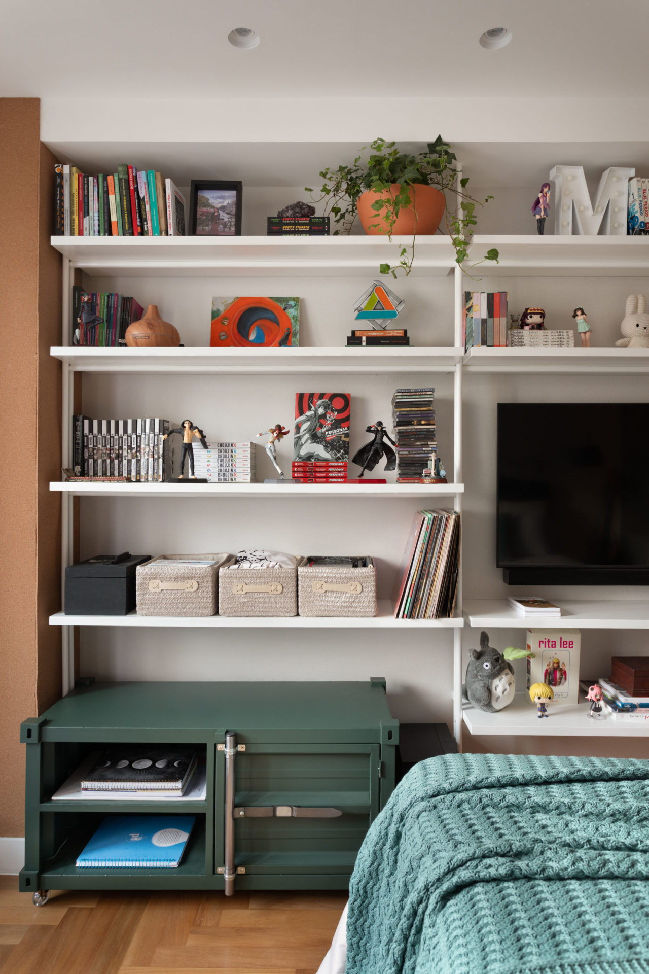na foto quarto com estante branca com tv, livros, fotos e vasos com plantas