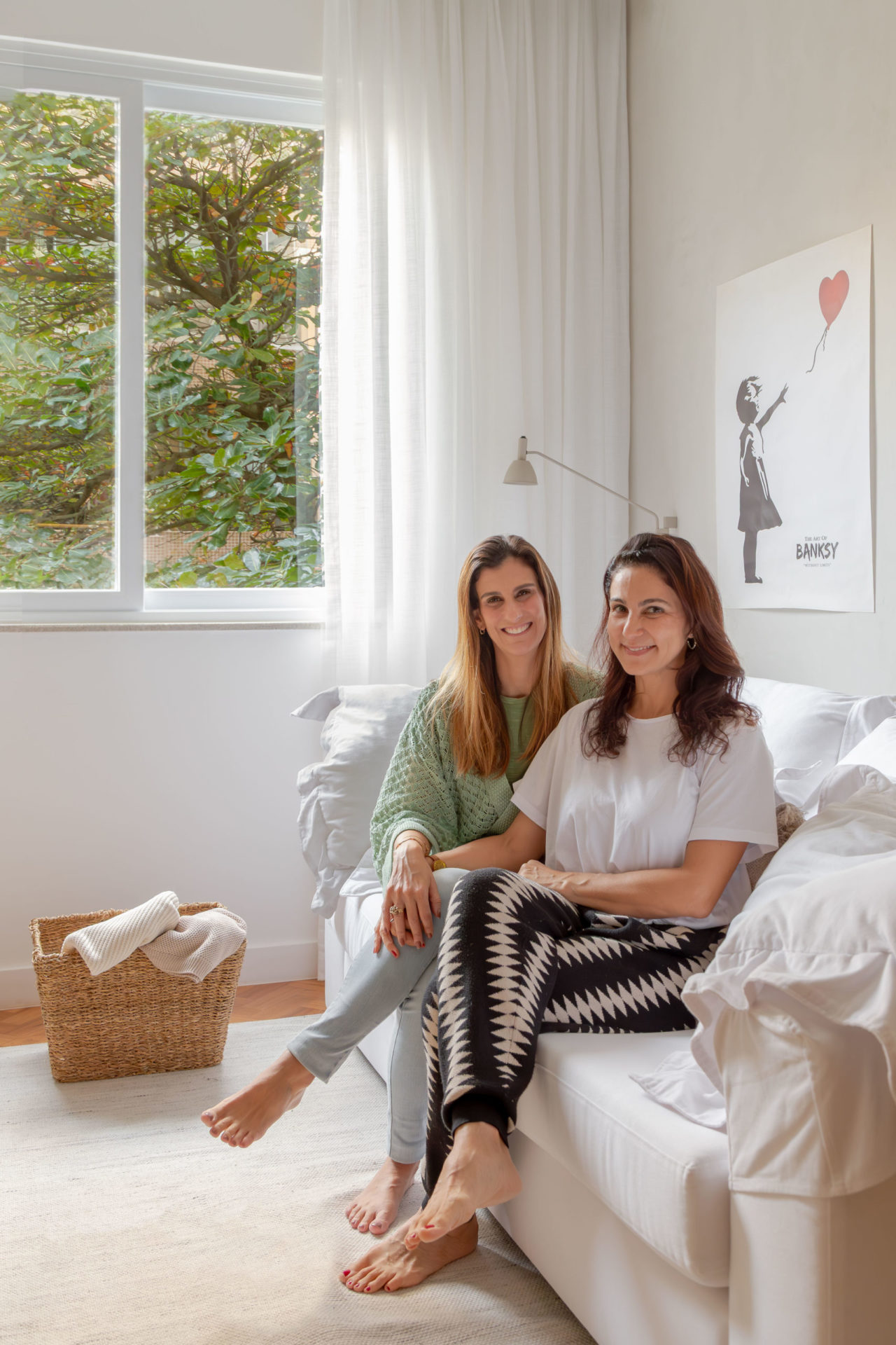 na foto duas mulheres sentadas em um sofá branco