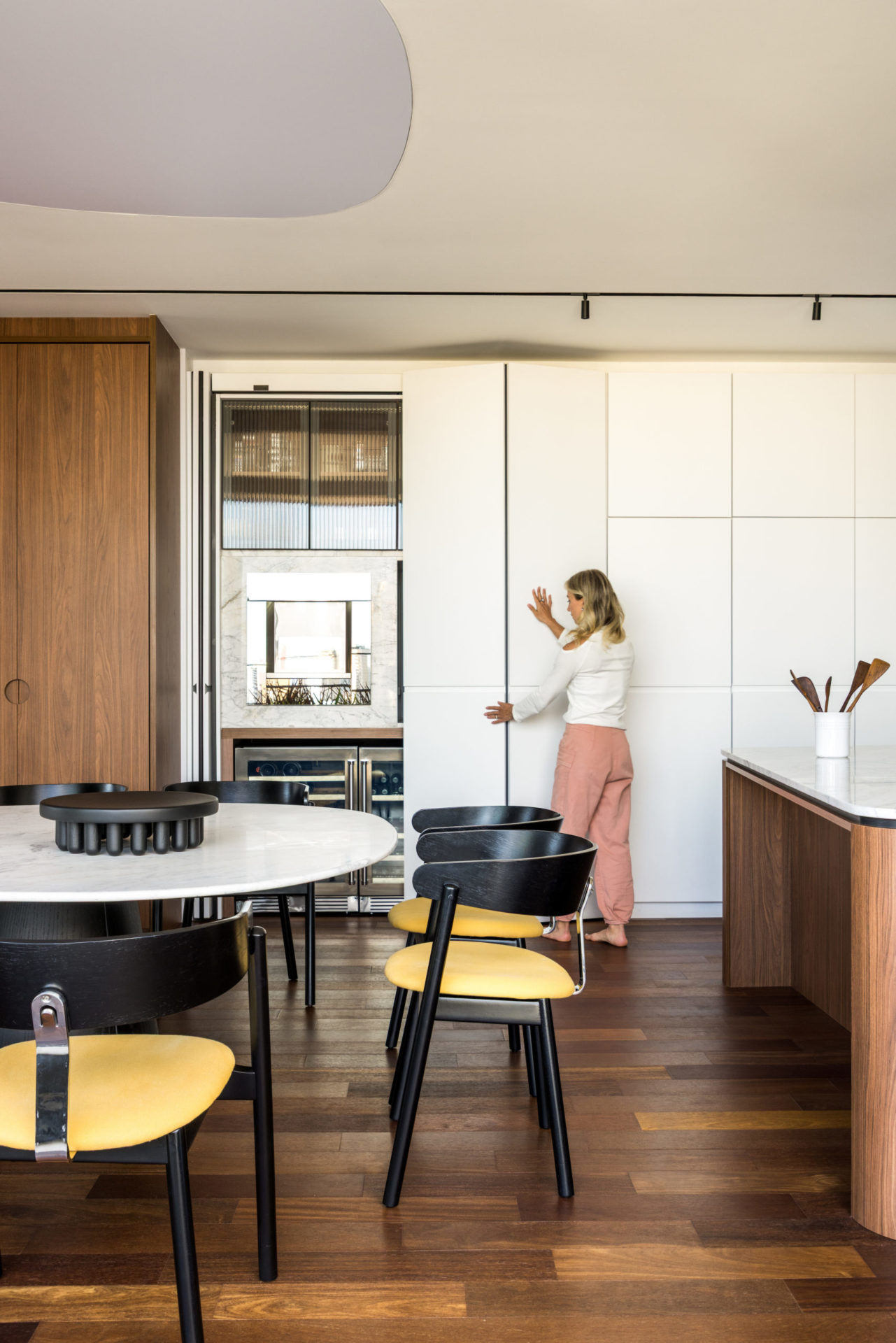 na foto mesa, cozinha e uma mulher abrindo uma porta escamoteada