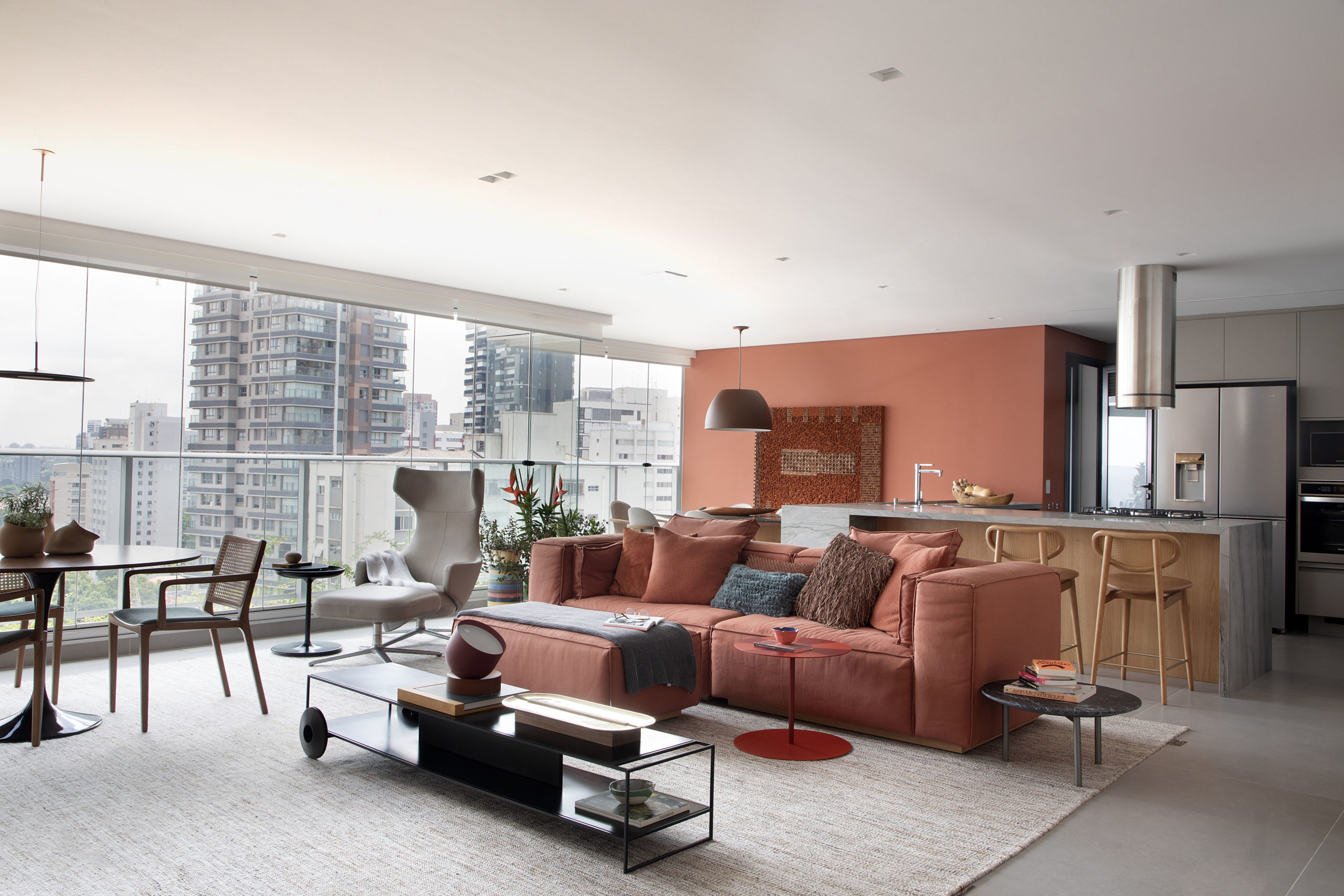 na foto está o living, uma grande janela e cozinha americana