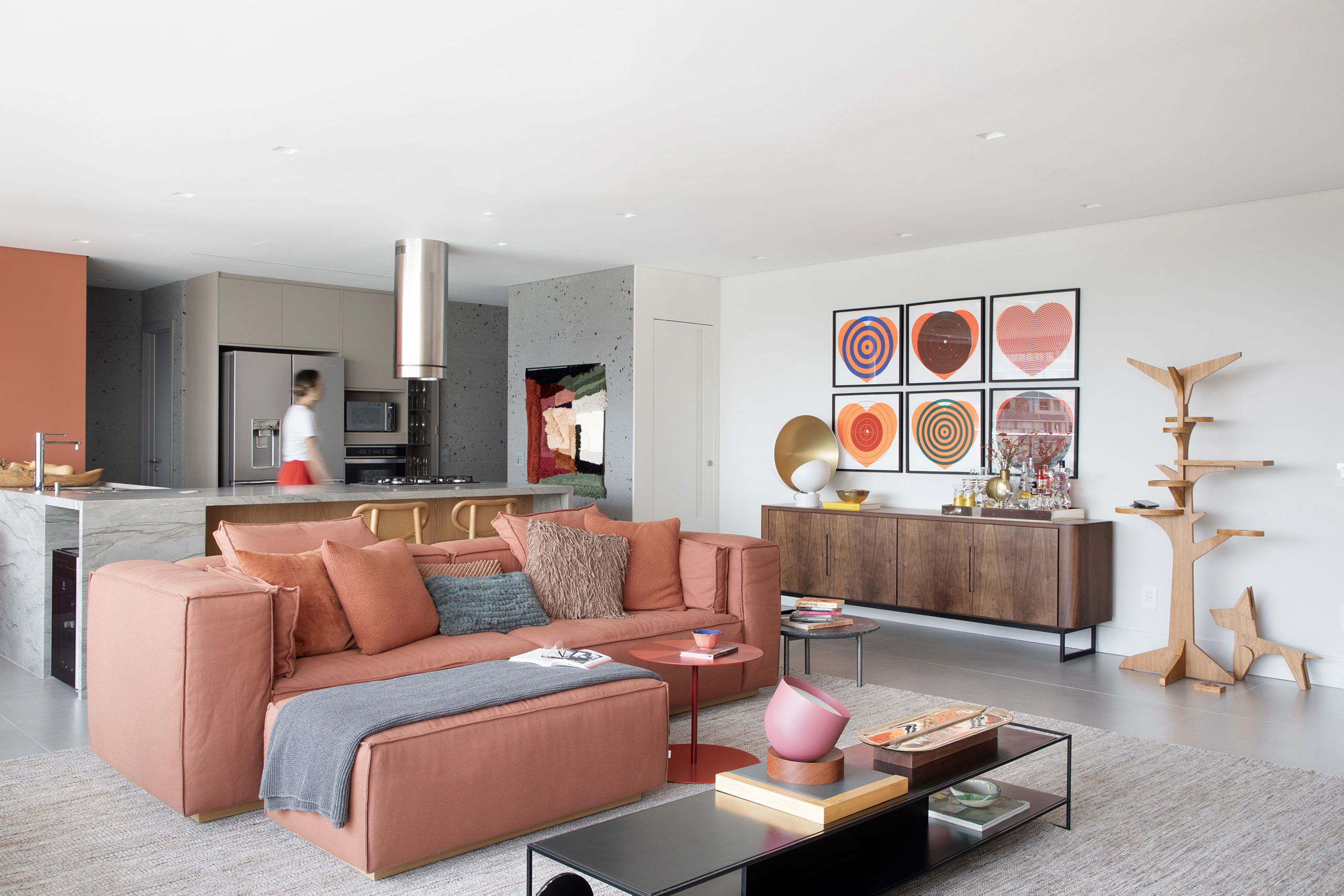 na foto sala com sofá em tom terroso, mesa de centro, bufe e vista para a cozinha americana