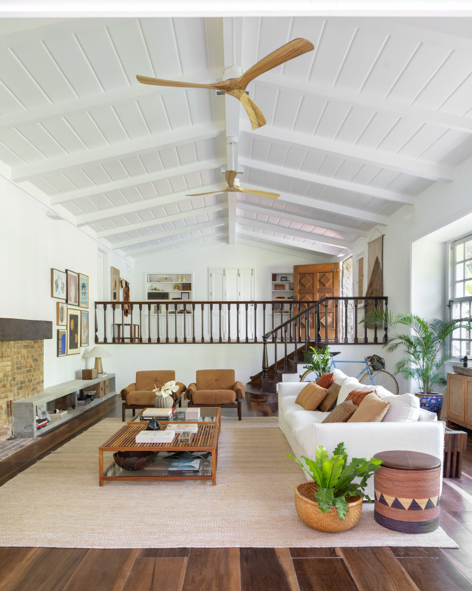 na foto sala com sofá, mesa de centro, escada, paredes brancas com quadros, grandes janelas