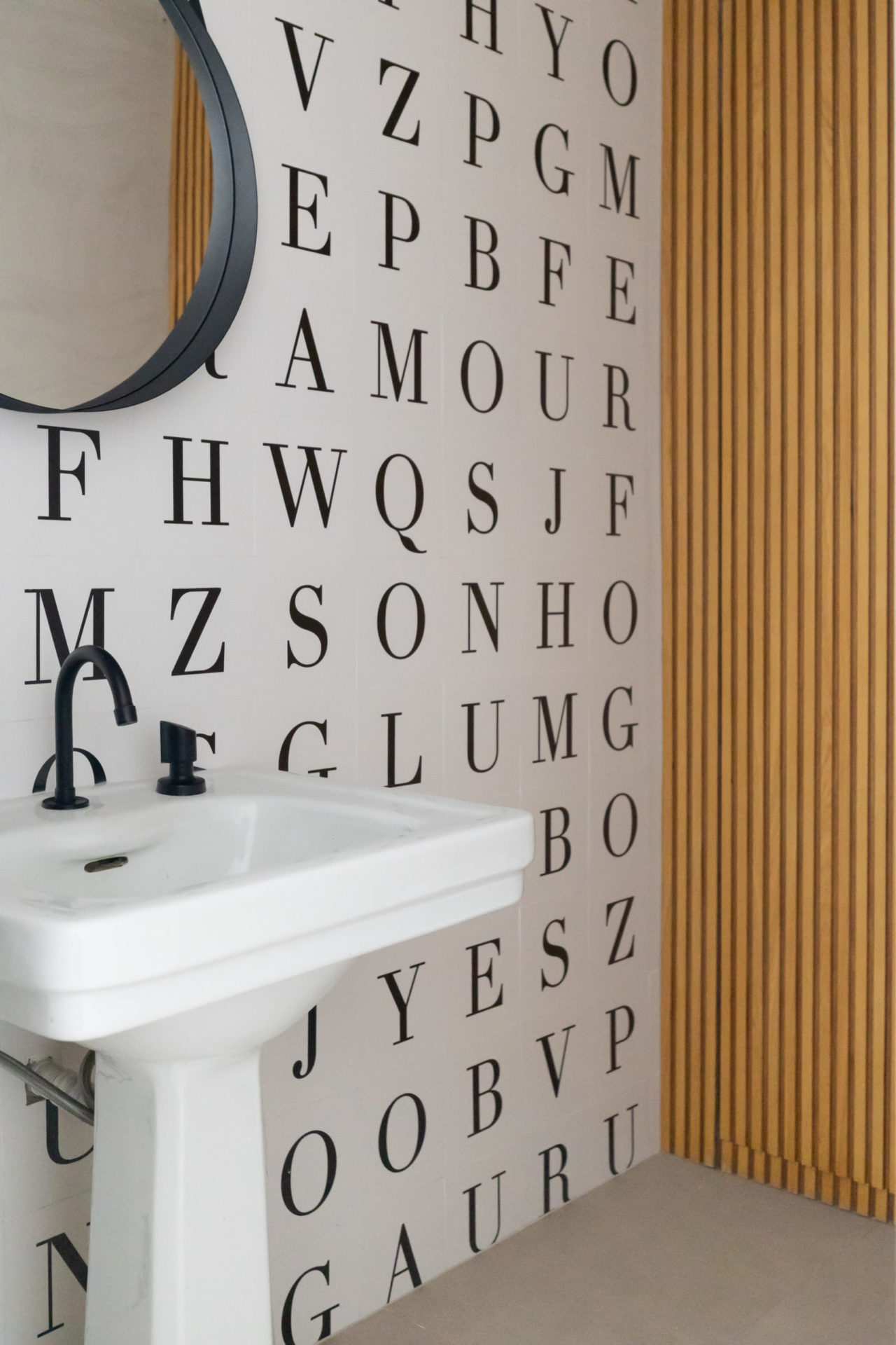 na foto lavabo com pia branca, espelho redondo e parede com letras