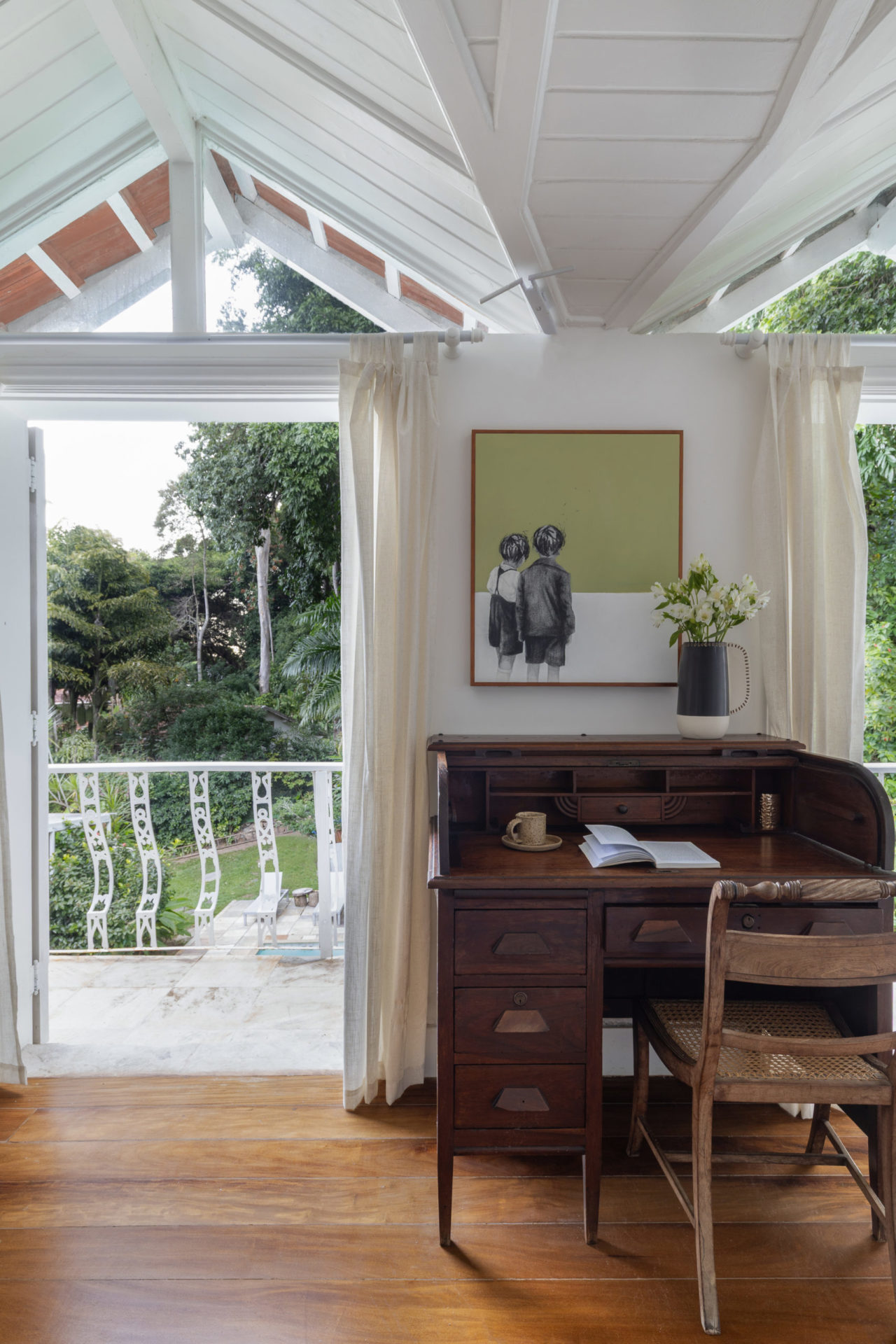 na foto escrivaninha de madeira, porta aberta para a varanda