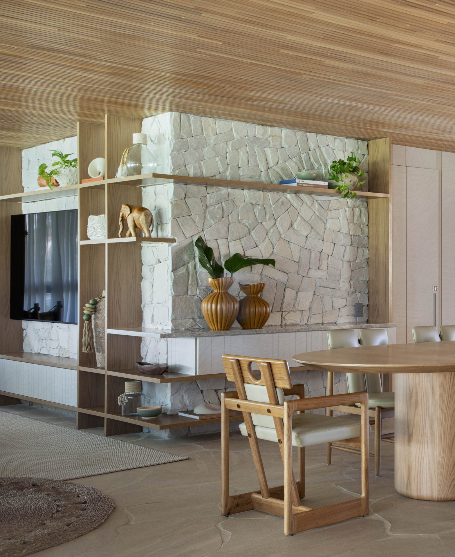 na foro sala com TV na parede, estante com objetos e parte de uma mesa