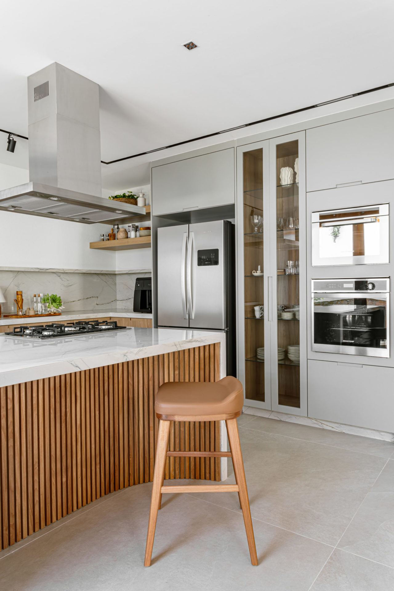 na foto cozinha com bancada, geladeira e fogão embutidos e armário