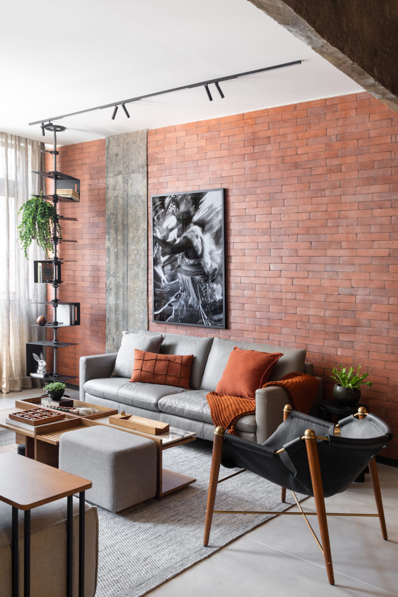 na foto sala de loft com estante escultural e paredes com tijolos