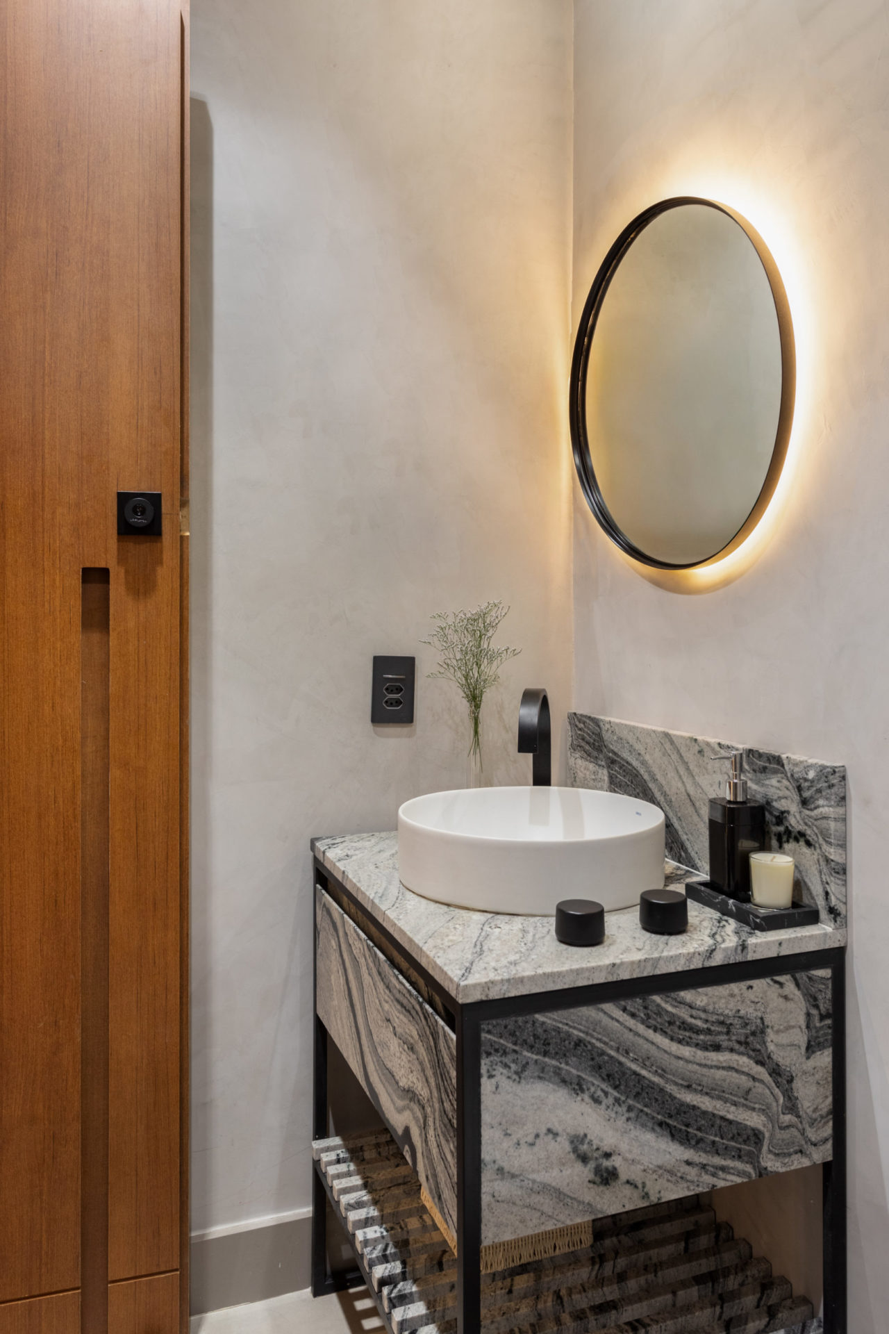 na foto lavabo com espelho redondo e com iluminação