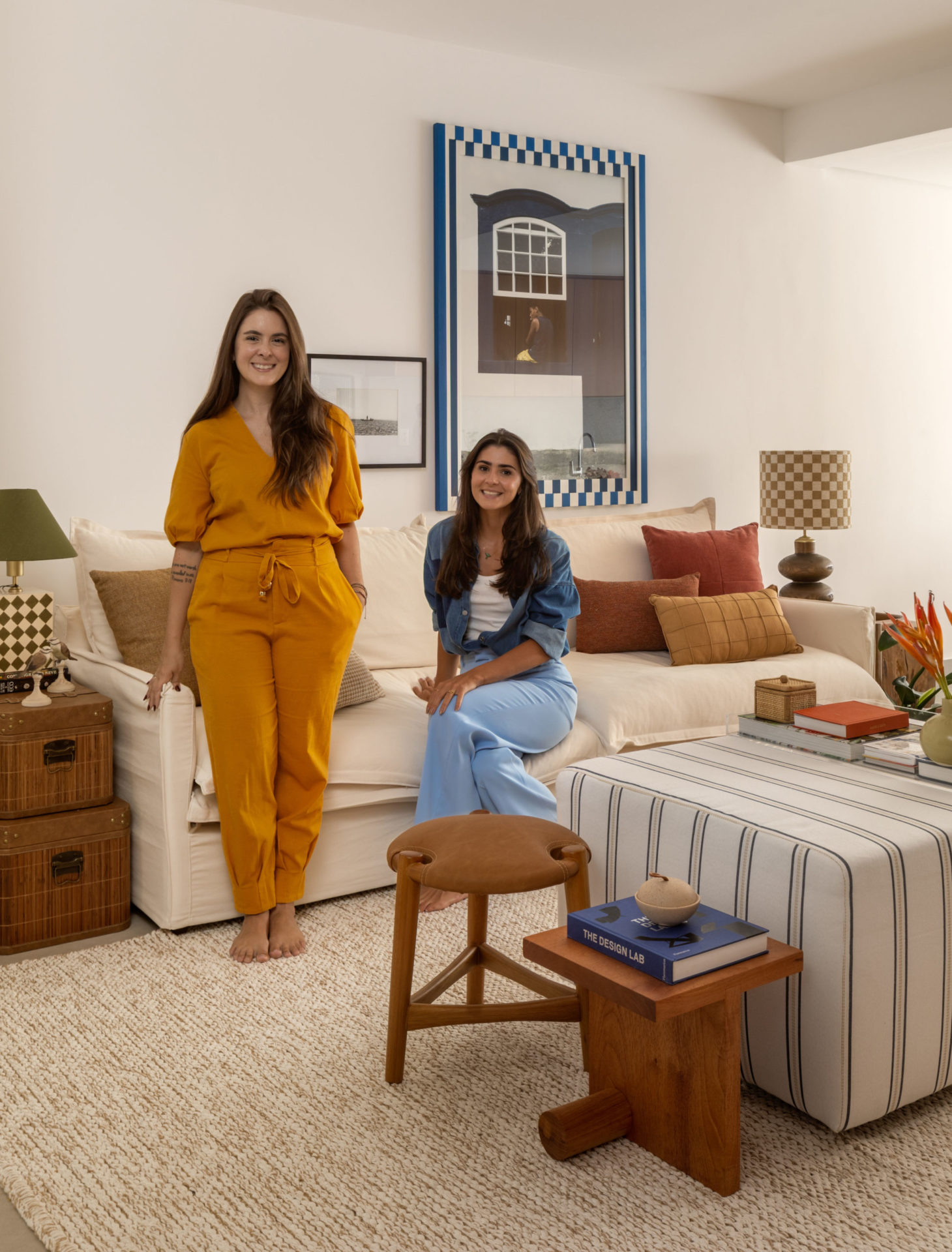 na foto duas mulheres brancas de cabelos castanhos, sendo que uma sentada e uma de pé