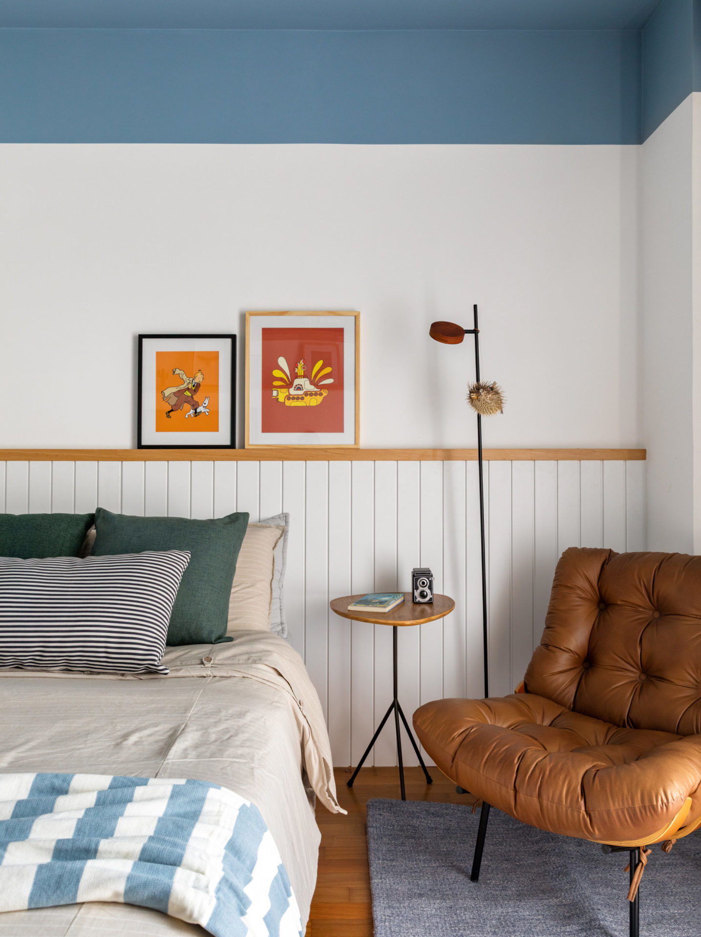 na foto quarto com paredes em branco e azul, cama, luminária de chão e poltrona de couro