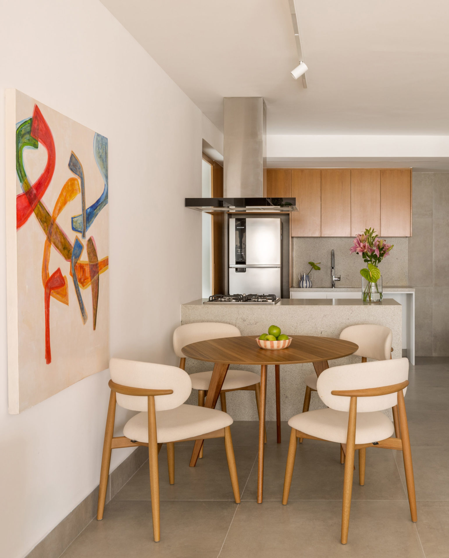 na foto mesa para quatro pessoas, quadro colorido na parede e cozinha ao fundo