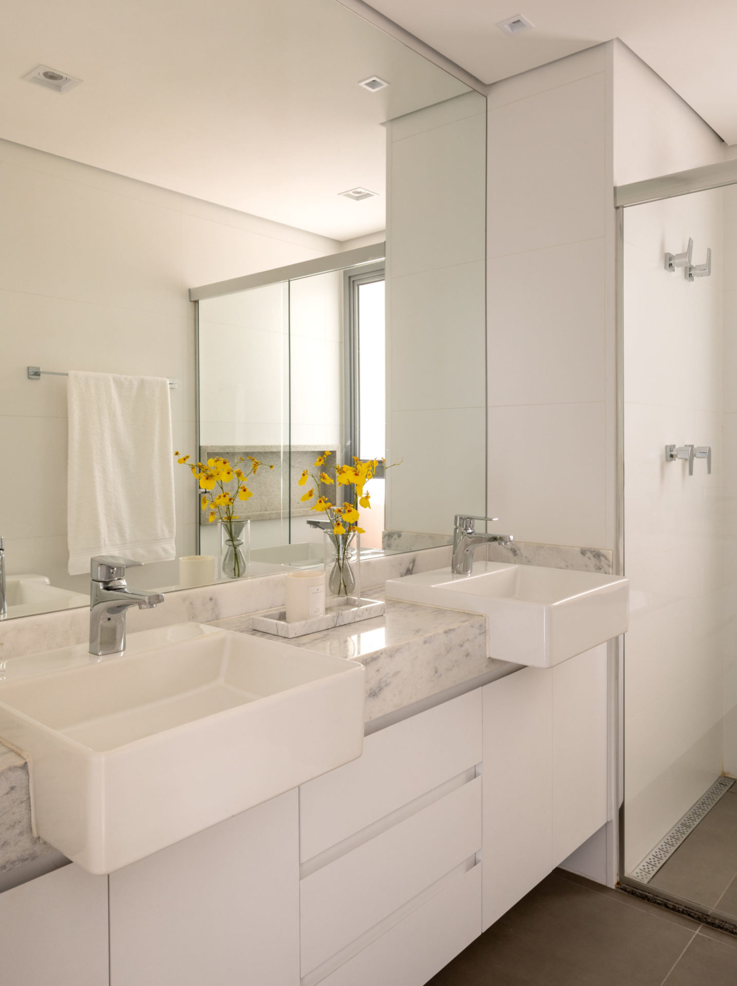 na foto banheiro toso na cor branca e flores amarelas na bancada