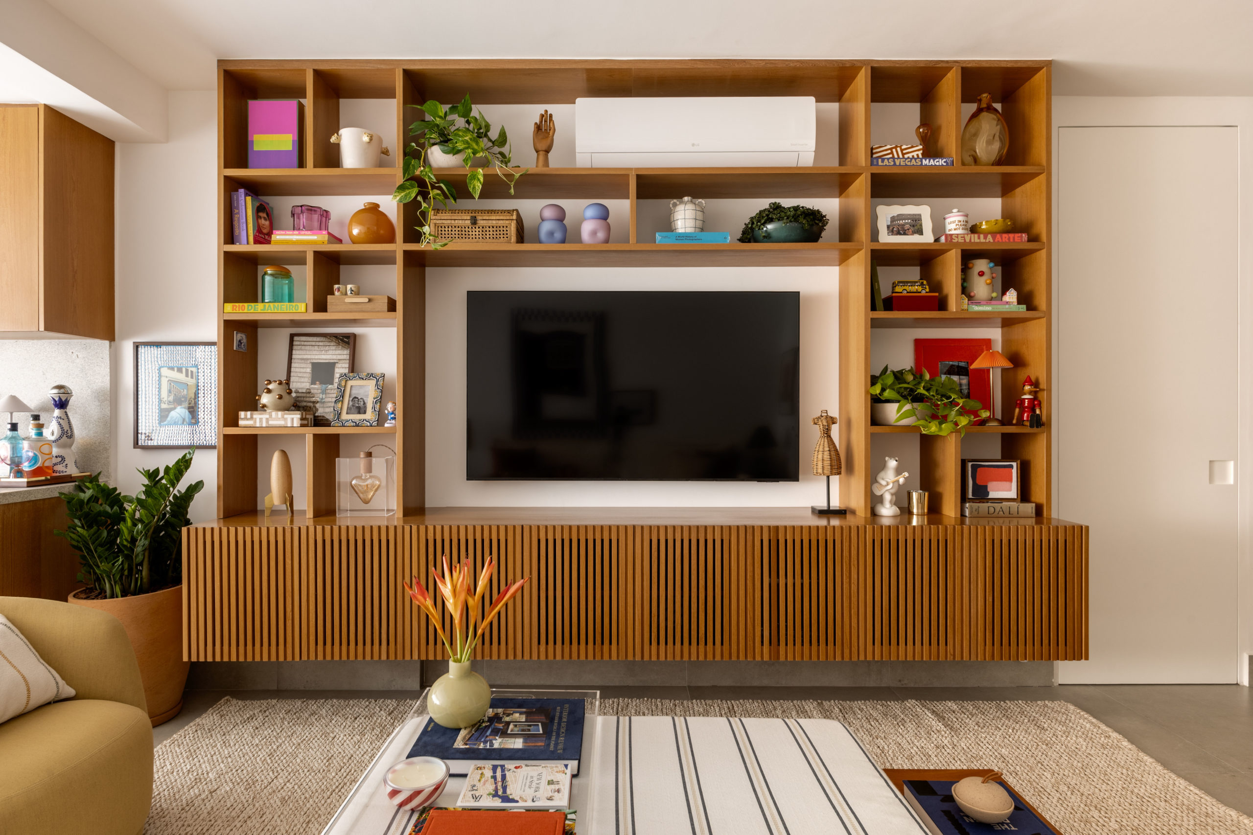 na foto uma sala com uma estante decorada com objetos afetivos e uma tv