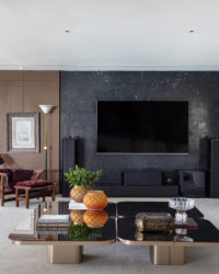 na foto sala ampla com TV na parede, mesa de centro espelhada e poltrona