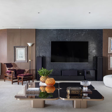 na foto sala ampla com TV na parede, mesa de centro espelhada e poltrona