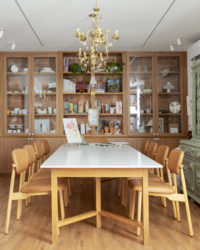 na foto mesa com seis cadeiras, duas estantes de madeira, lustre de ferro e espelho com moldura vermelha